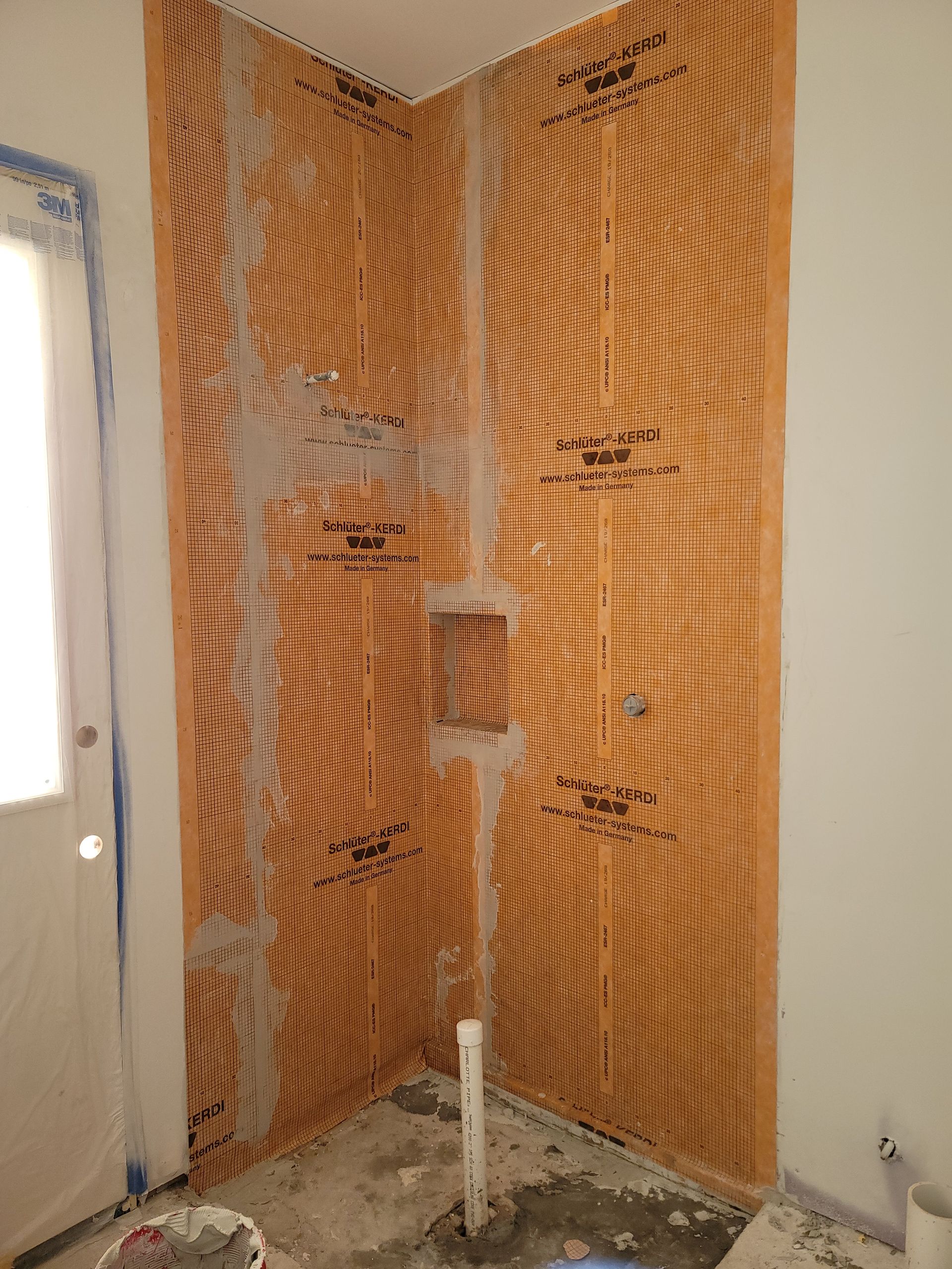 Partially demolished bathroom wall with exposed orange insulation and plumbing pipe