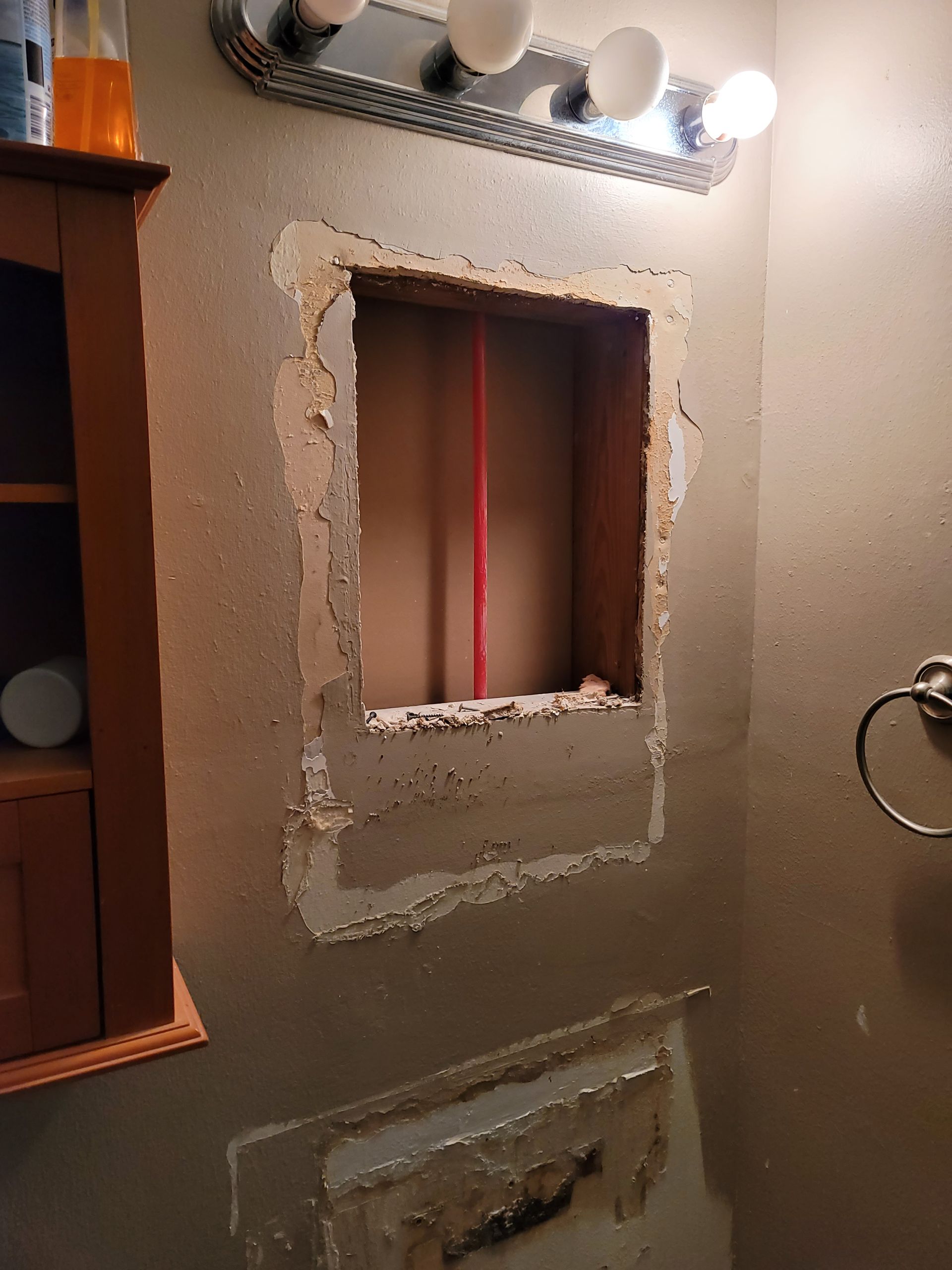 Bathroom wall with rough-cut square opening above a sink and vanity lights.