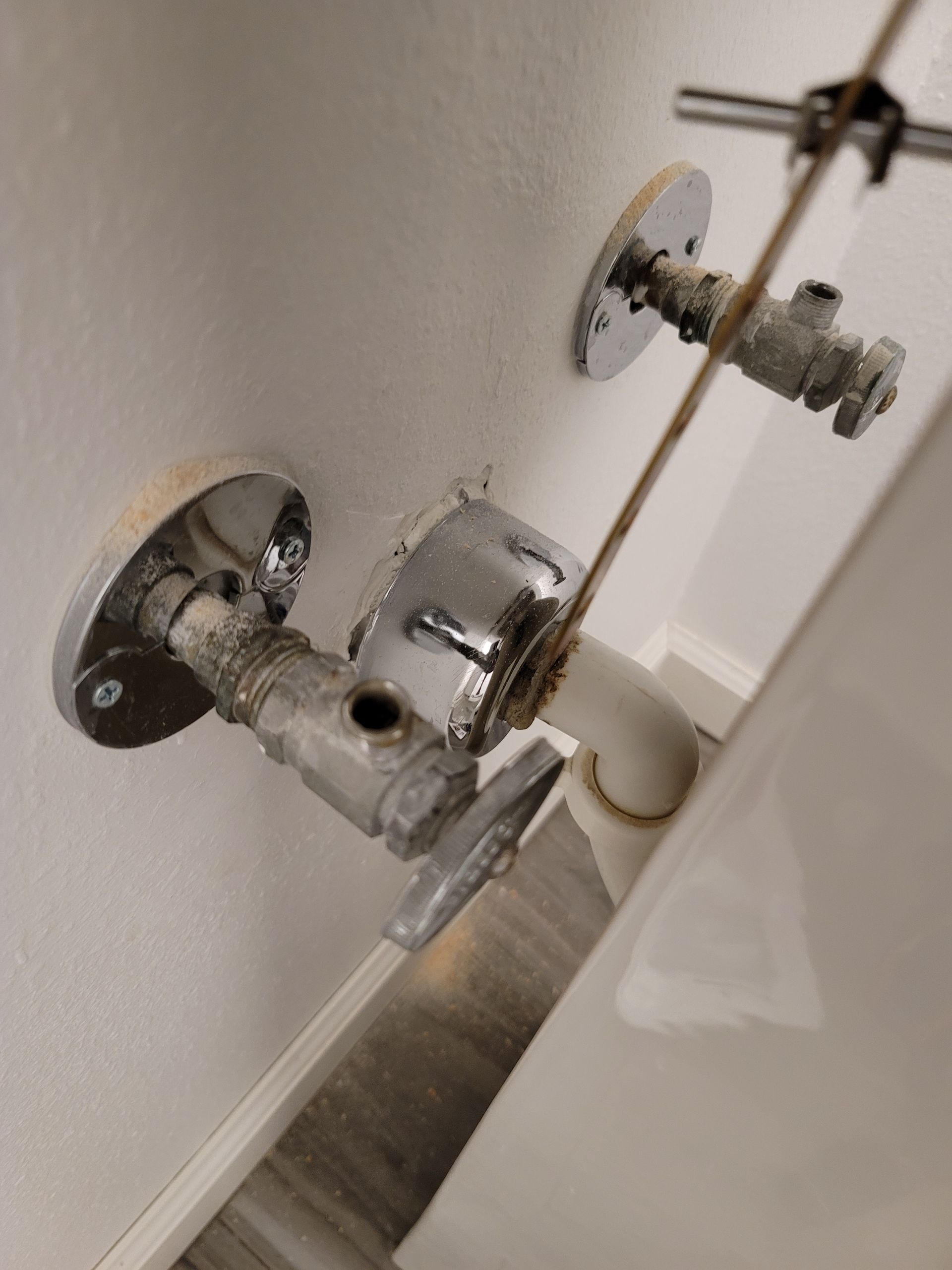 Close-up of wall-mounted plumbing fittings and valve pipes beside a white surface.
