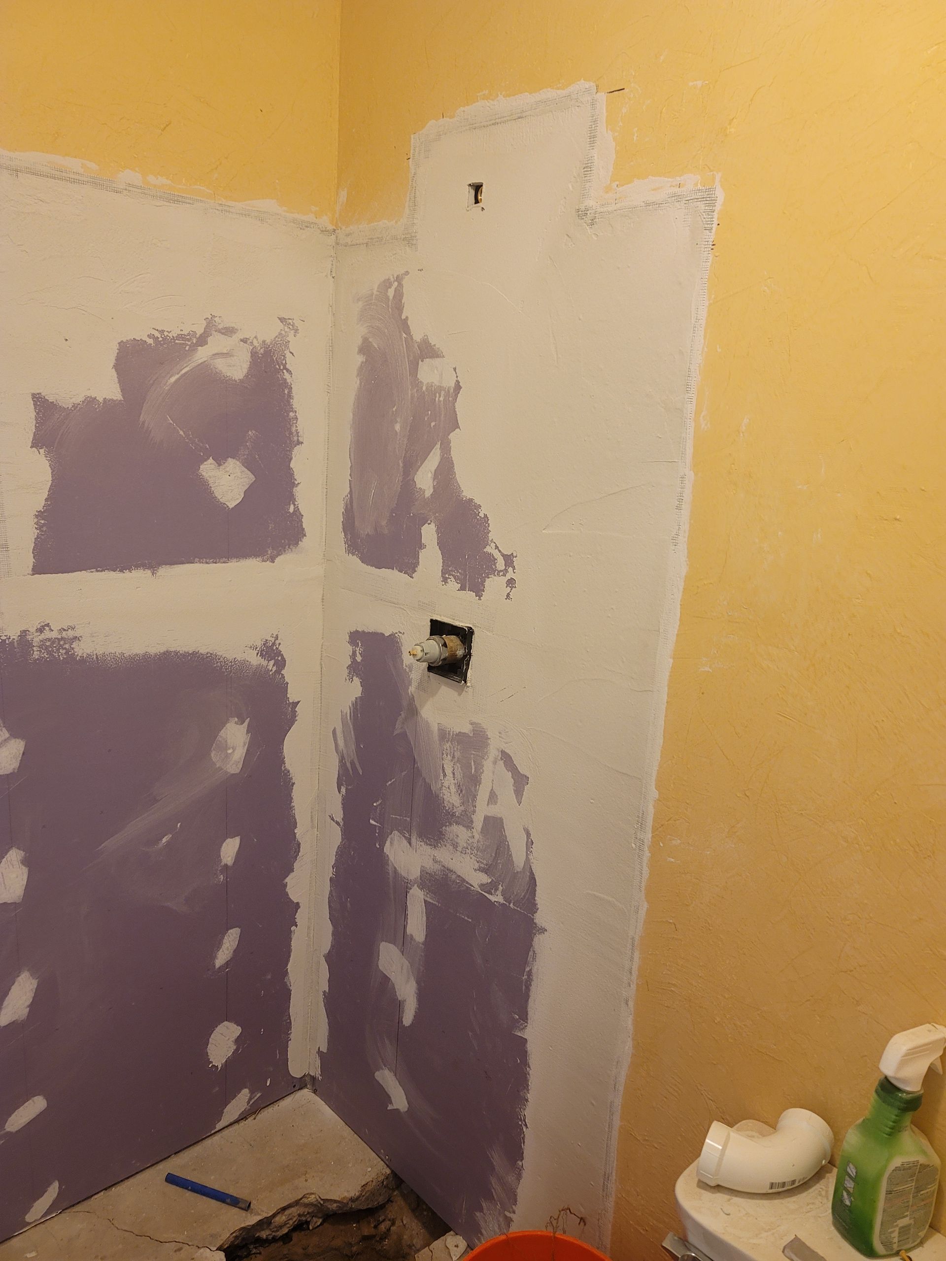 Partially painted bathroom wall with purple patching, white center strip, and a shower fixture on the right