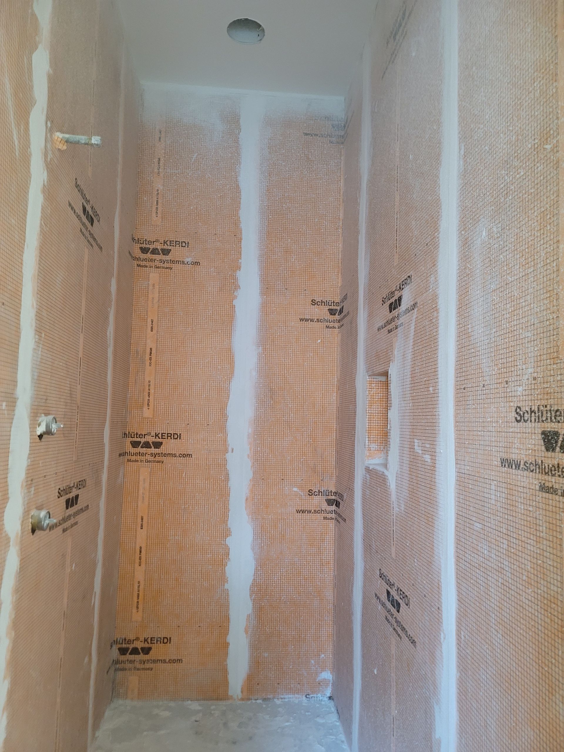 Narrow shower stall with white waterproof membrane and orange insulation boards on the walls
