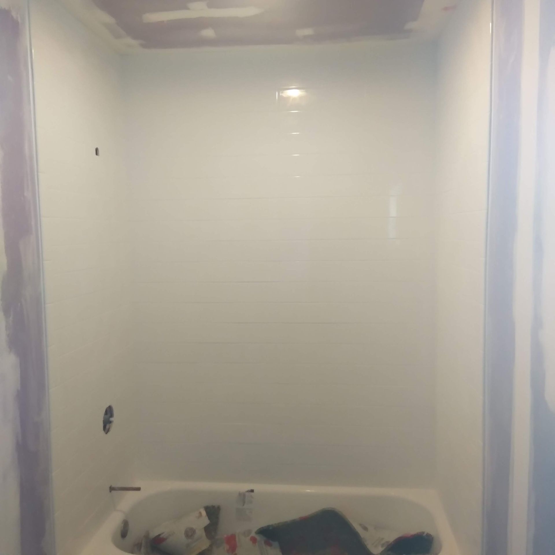 White shower stall under construction with tiled walls and a bathtub below