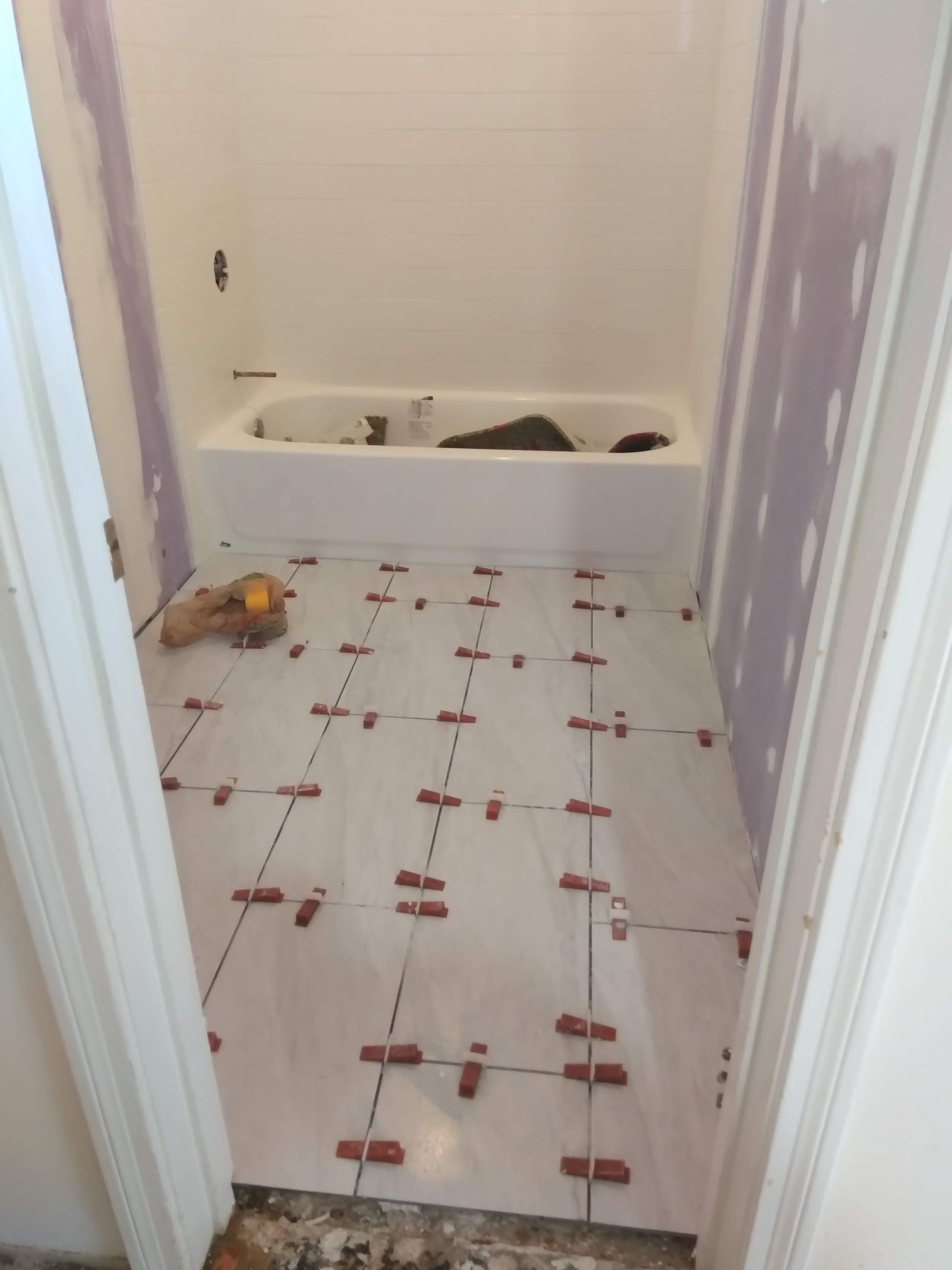Bathroom under renovation with white tile floor, unfinished walls, and a bathtub at the far end.