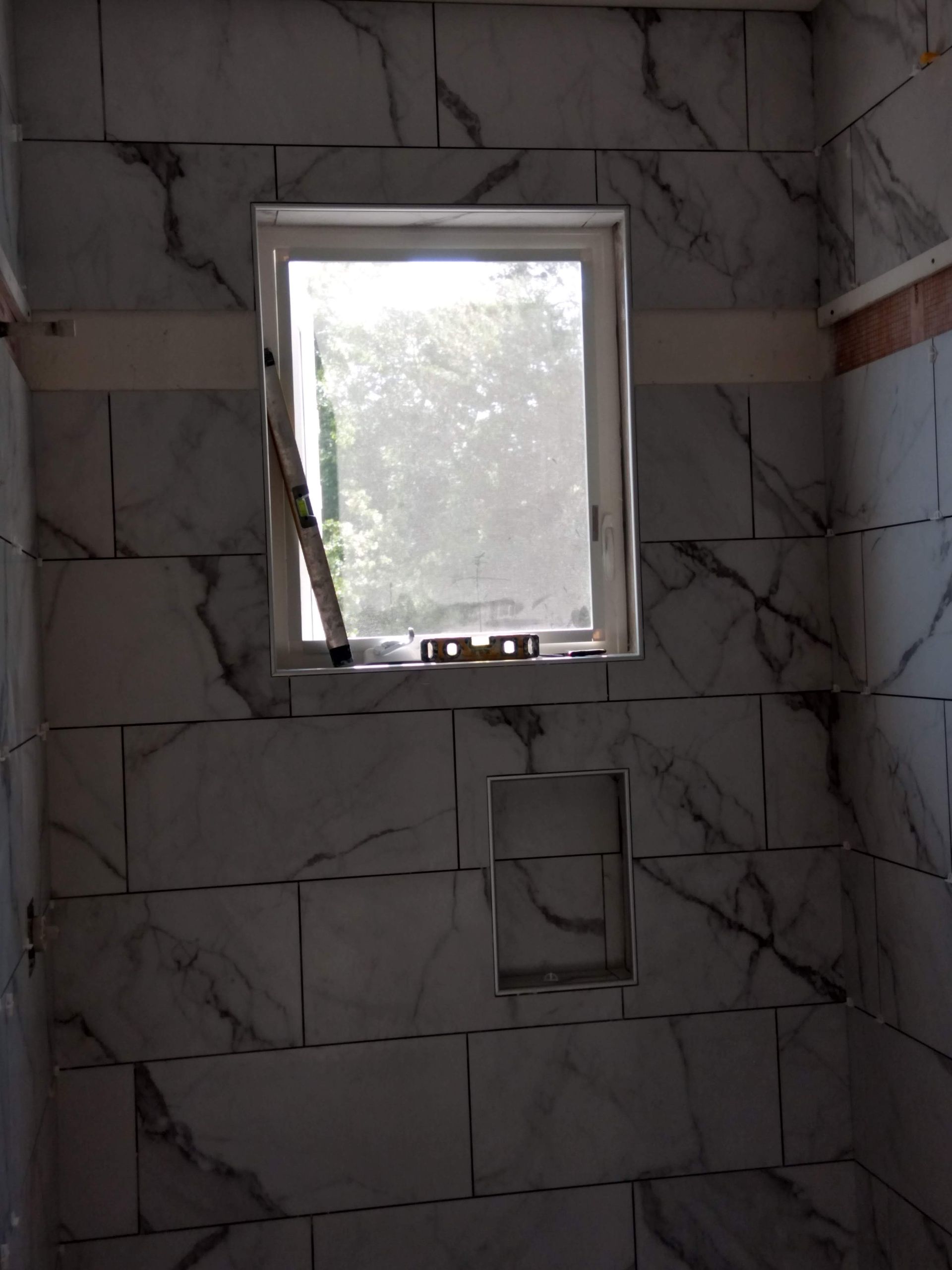 Tiled shower stall with a small frosted window letting in daylight.