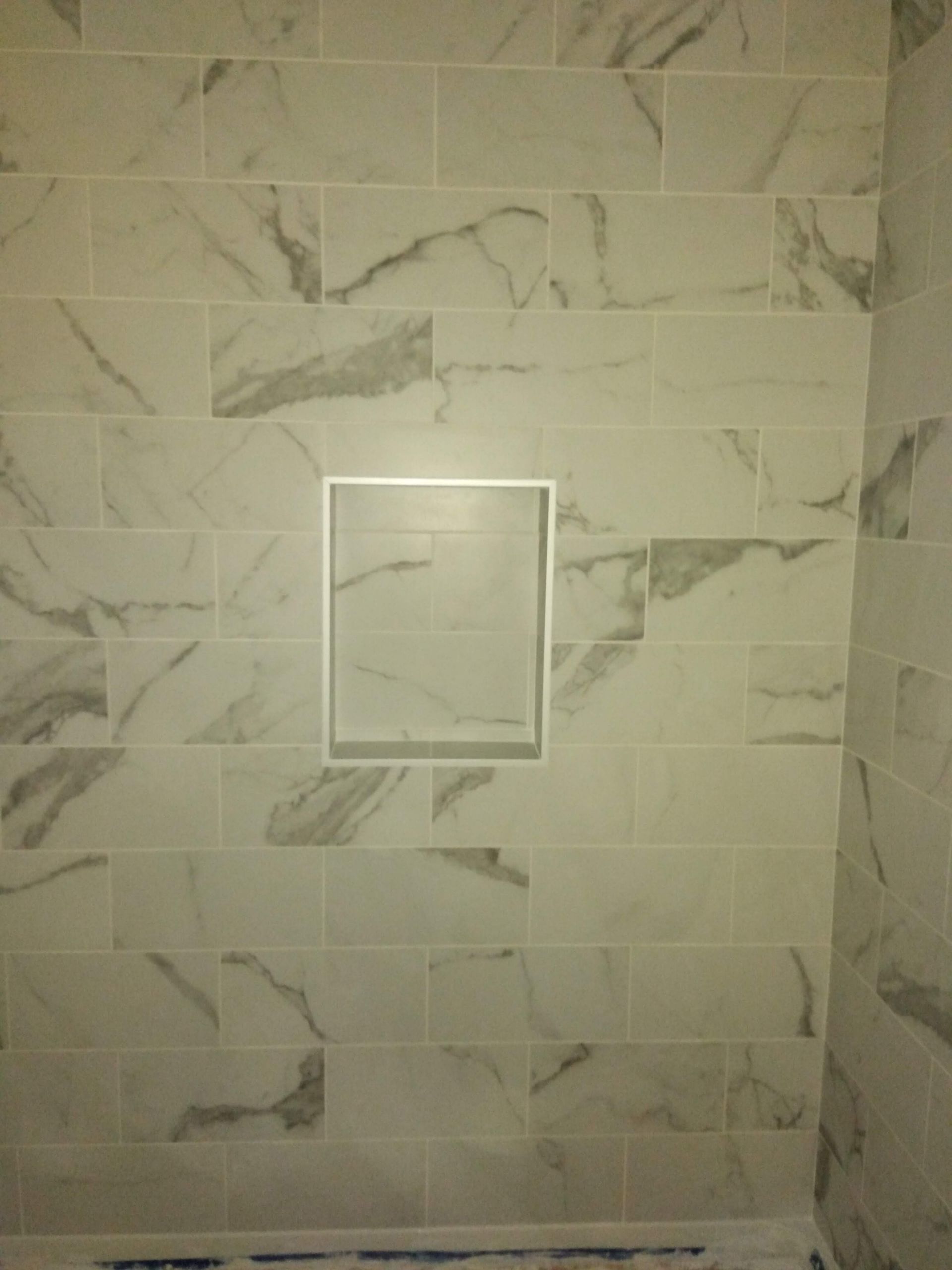 Marble-tiled shower wall with a small recessed niche or panel in the center