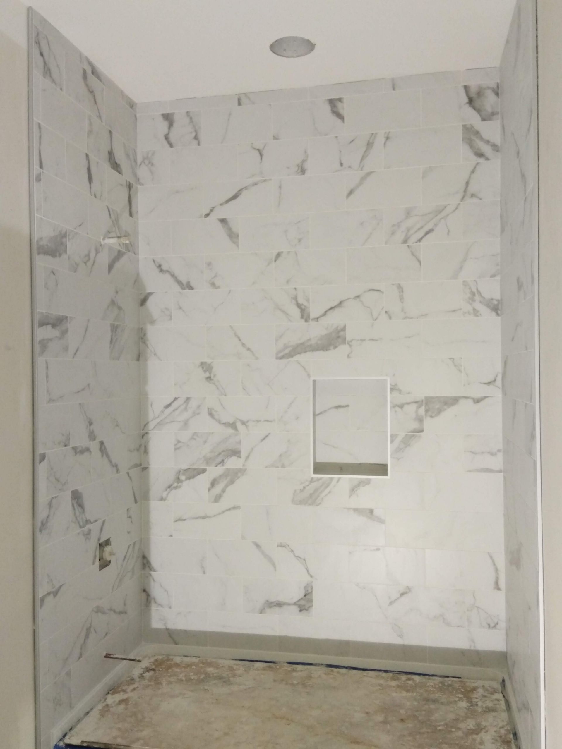Empty tiled shower stall with marble-pattern walls and a recessed niche.