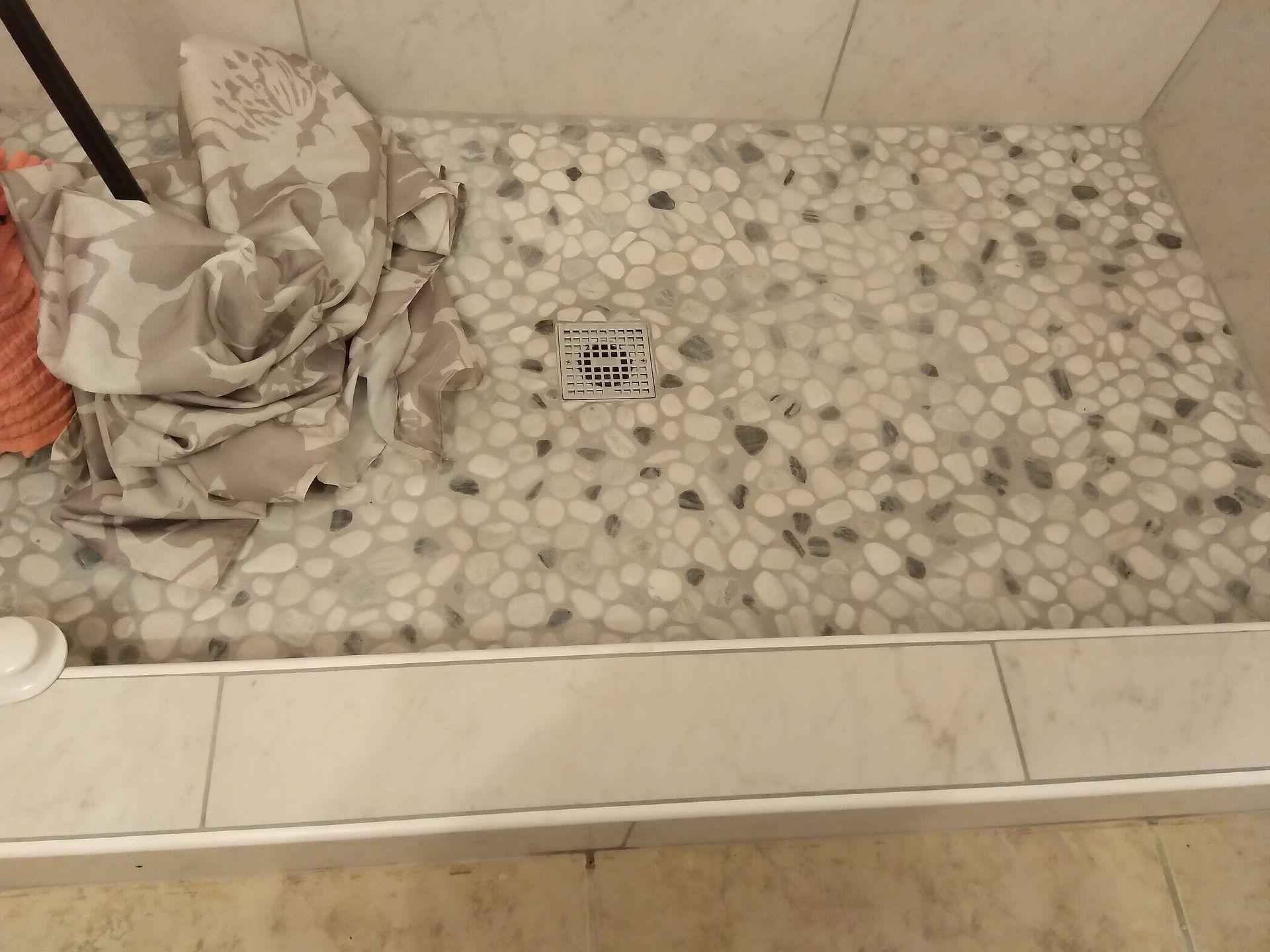 Shower floor with pebble-style tile, drain, and a crumpled cloth in the corner