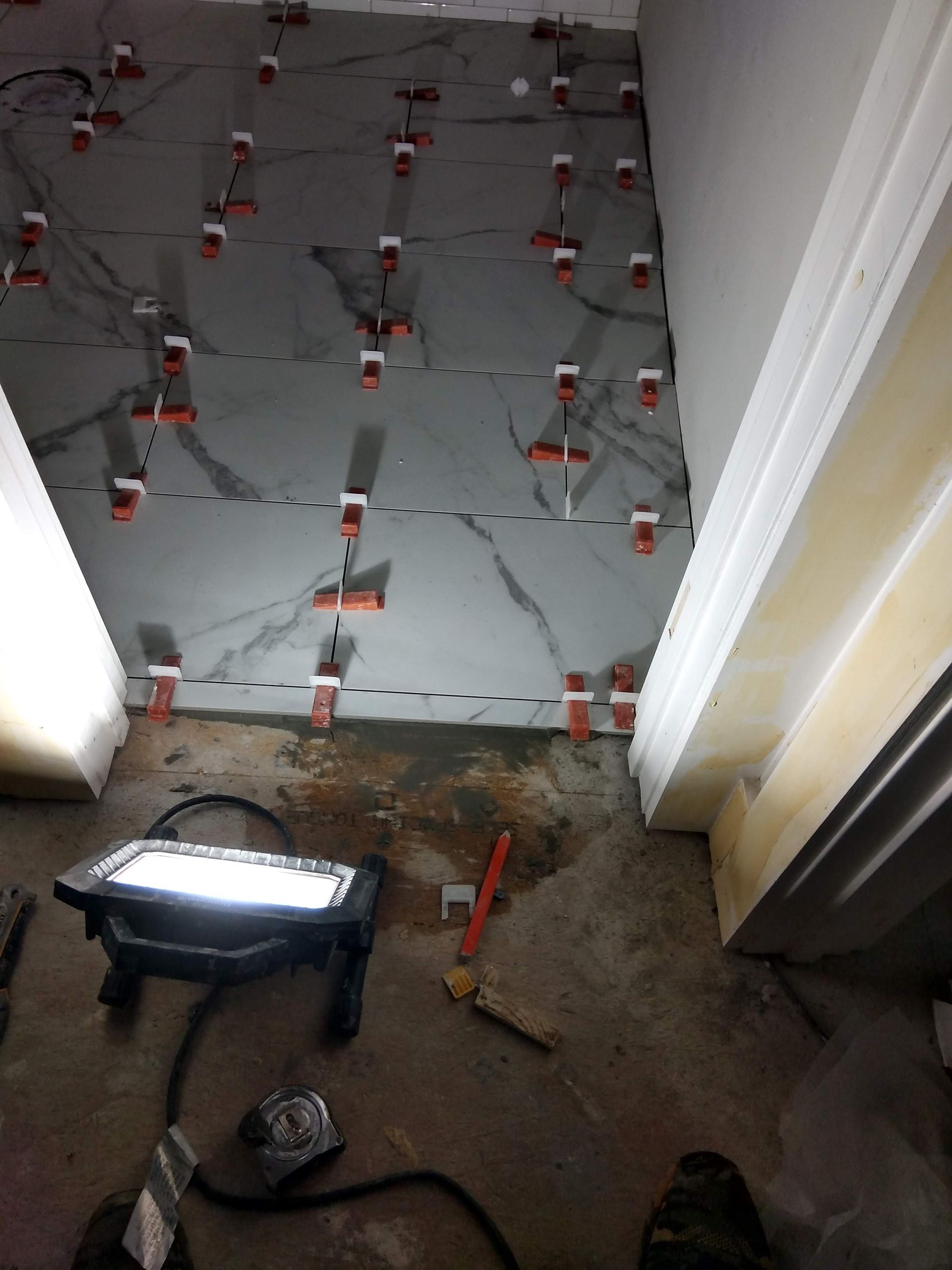 Bathroom floor under tile leveling clips, with a work light and tools during renovation.