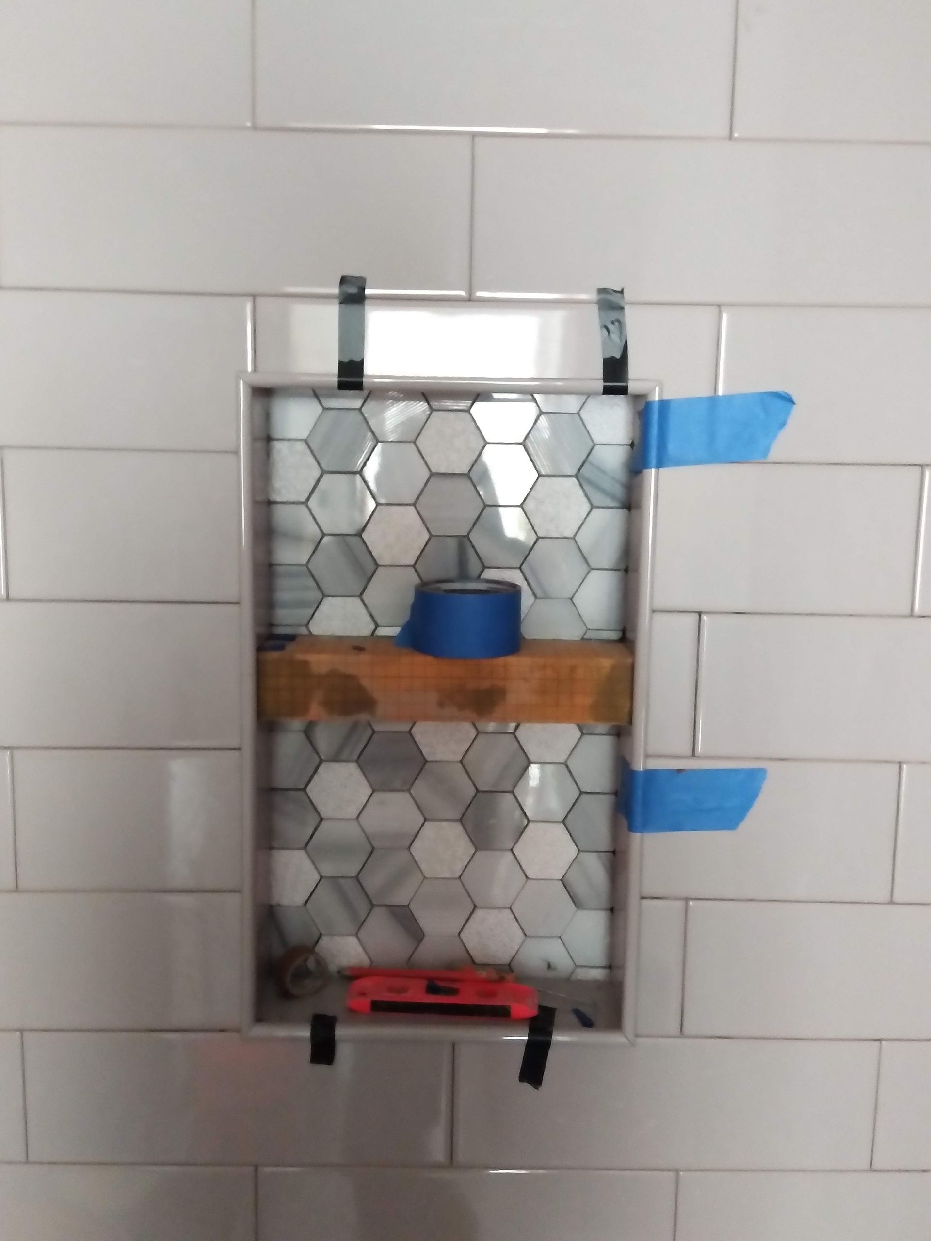 Wall-mounted hex-tiled soap dispenser with blue handles on a tiled bathroom wall