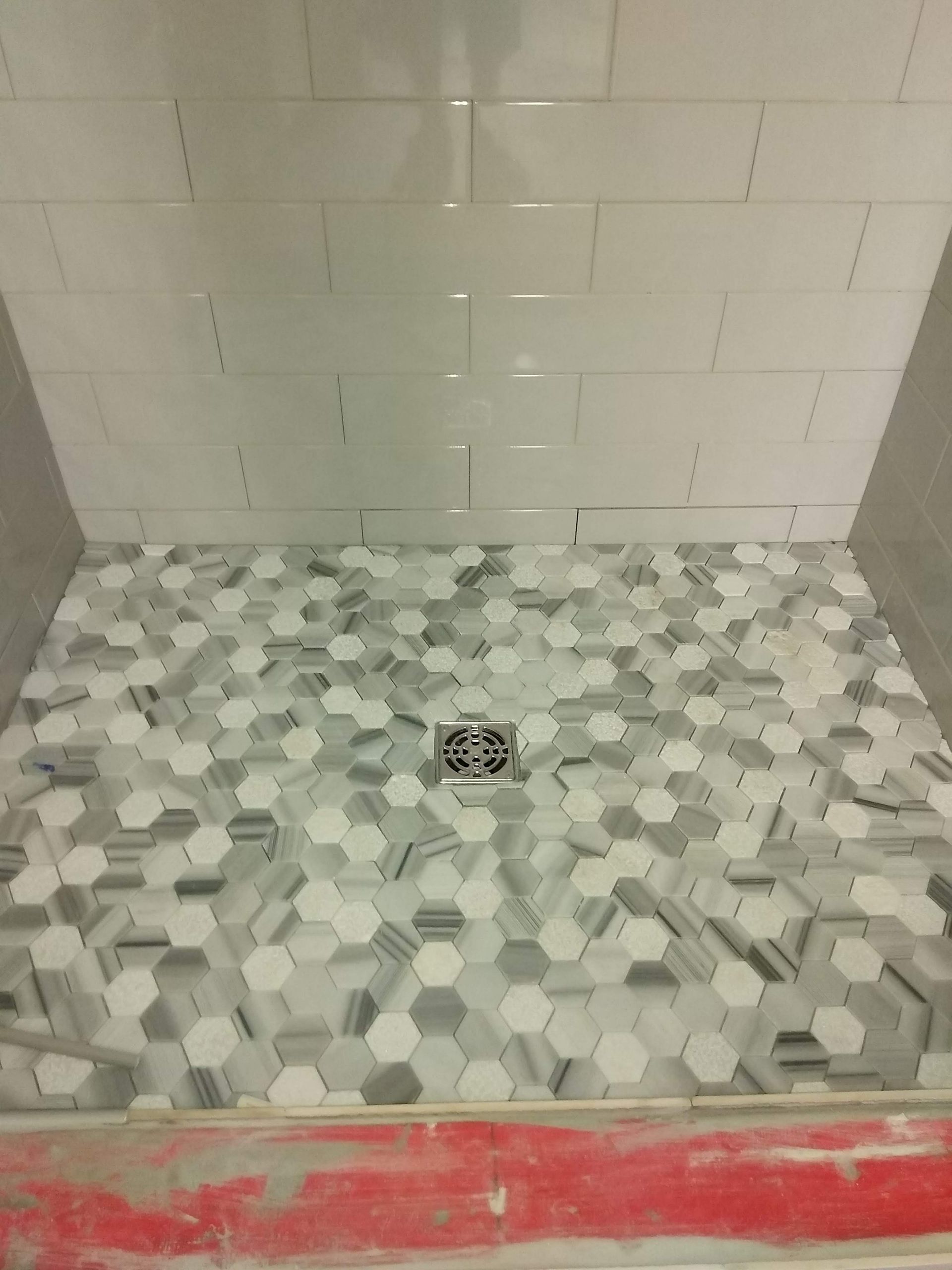 Tiled shower floor with hexagonal mosaic tile and a center drain, unfinished with red threshold at the front