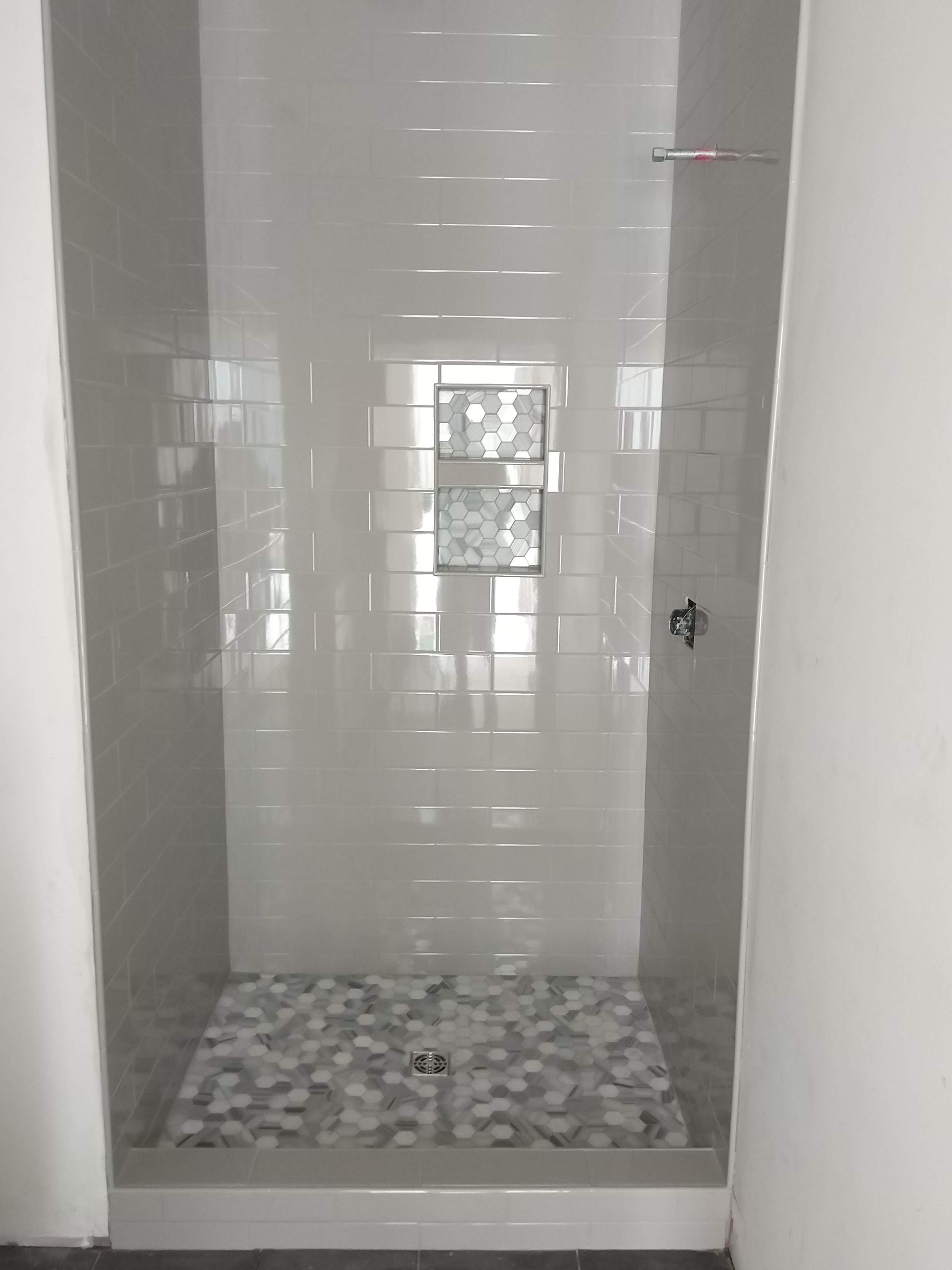 Empty tiled shower stall with mosaic floor and small window.