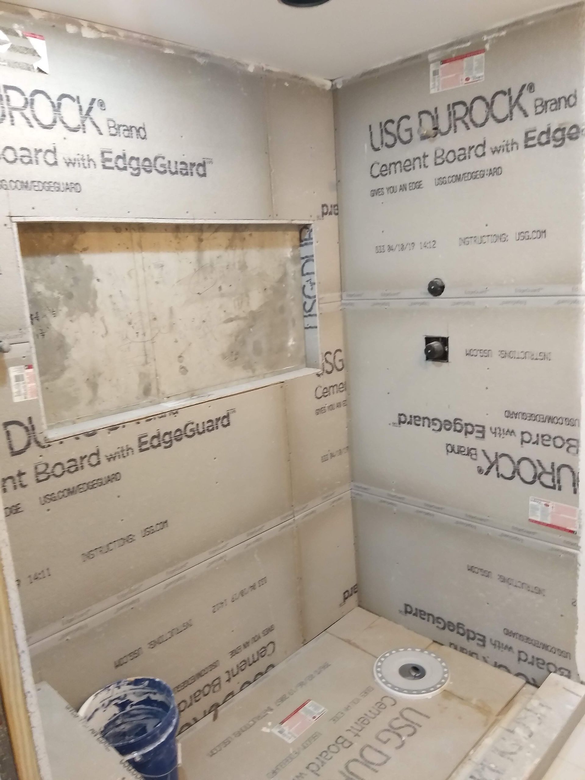 Bathroom under renovation with waterproof wall panels, unfinished shower, and construction materials on the floor