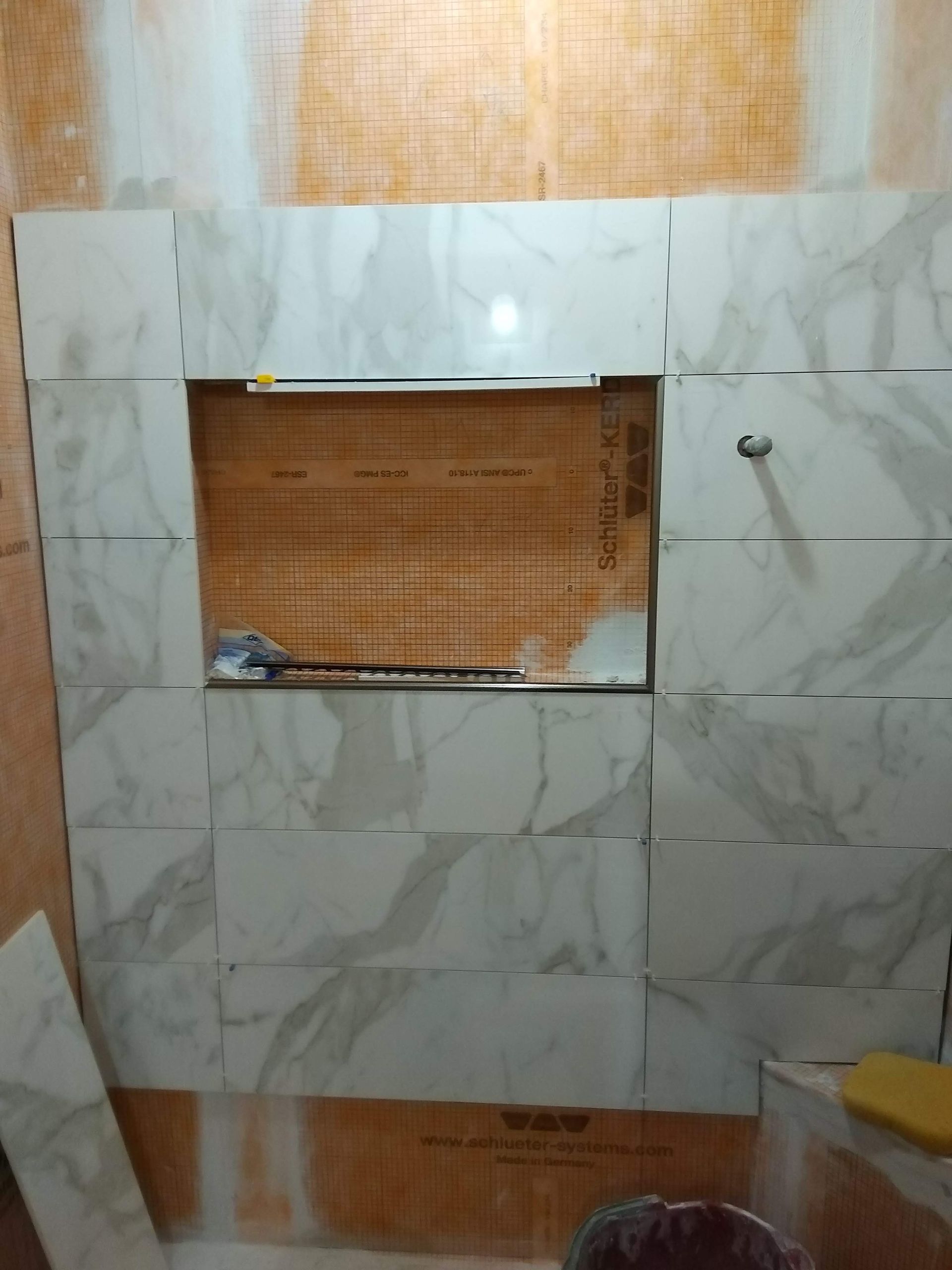 Tiled bathroom wall with a recessed shelf and exposed orange mesh in the center opening