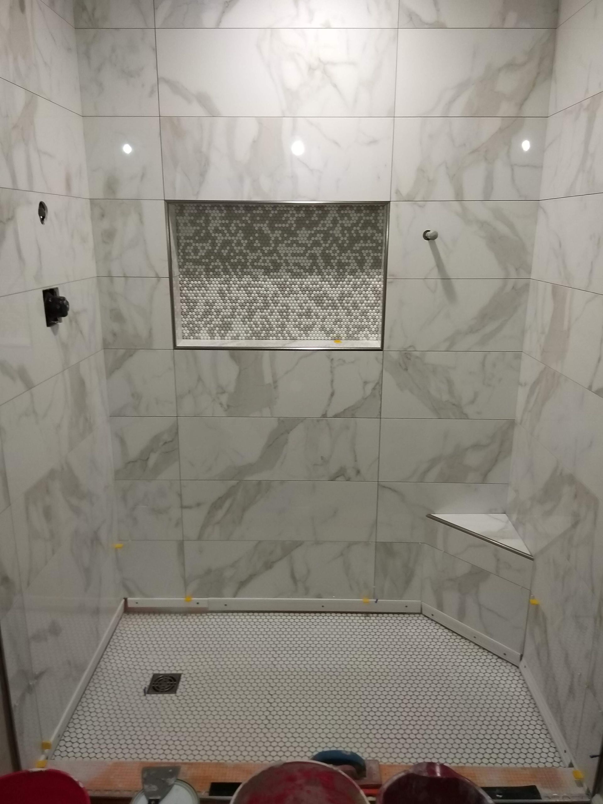 Empty tiled shower stall with a drain, bench shelf, and recessed niche.