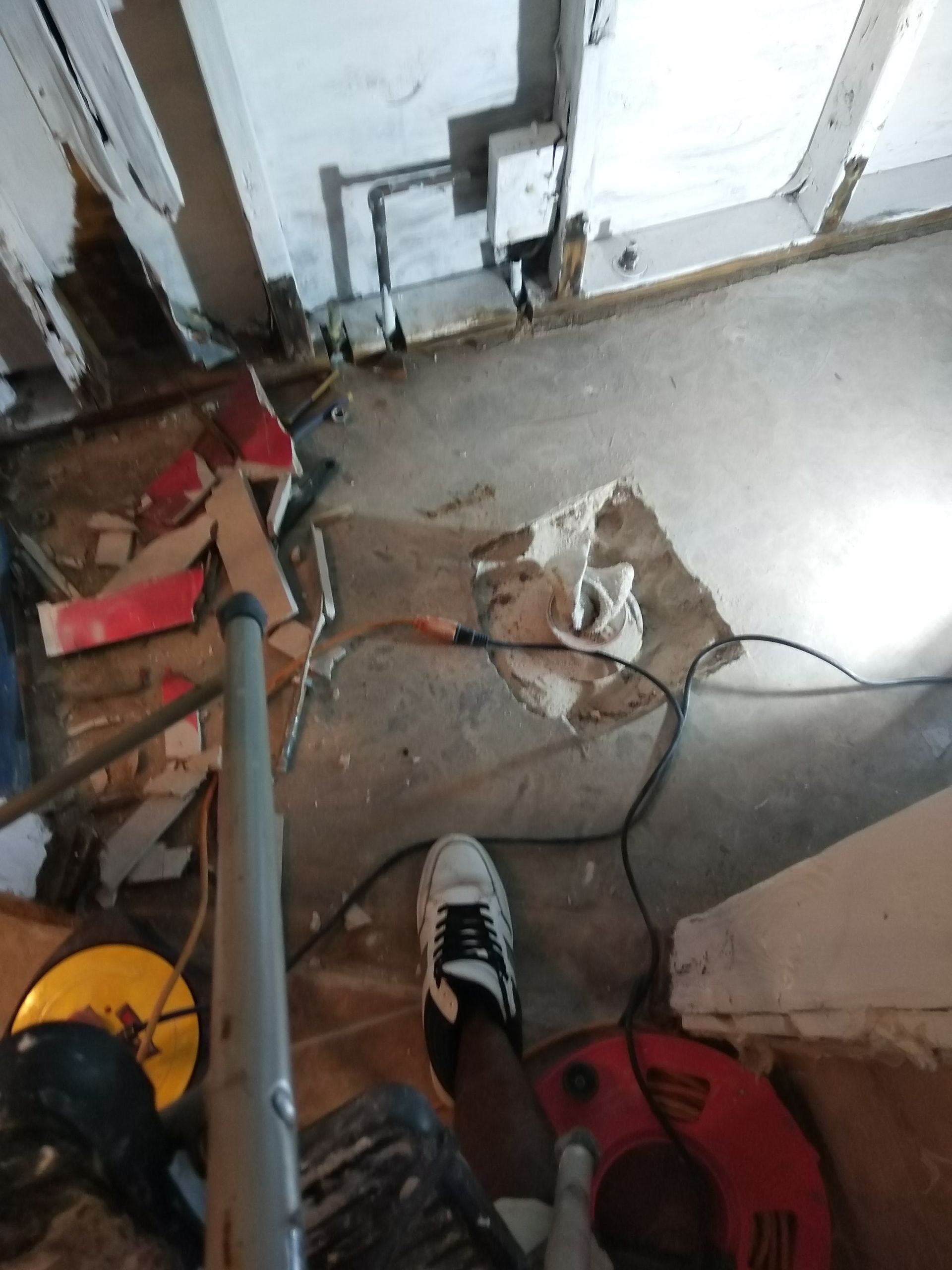 Messy indoor floor with tools, cords, and scattered debris near a white door.