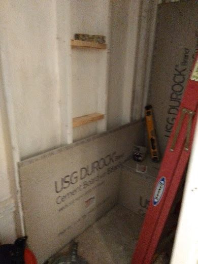 Construction site with drywall, ladder, and tools in a narrow unfinished room