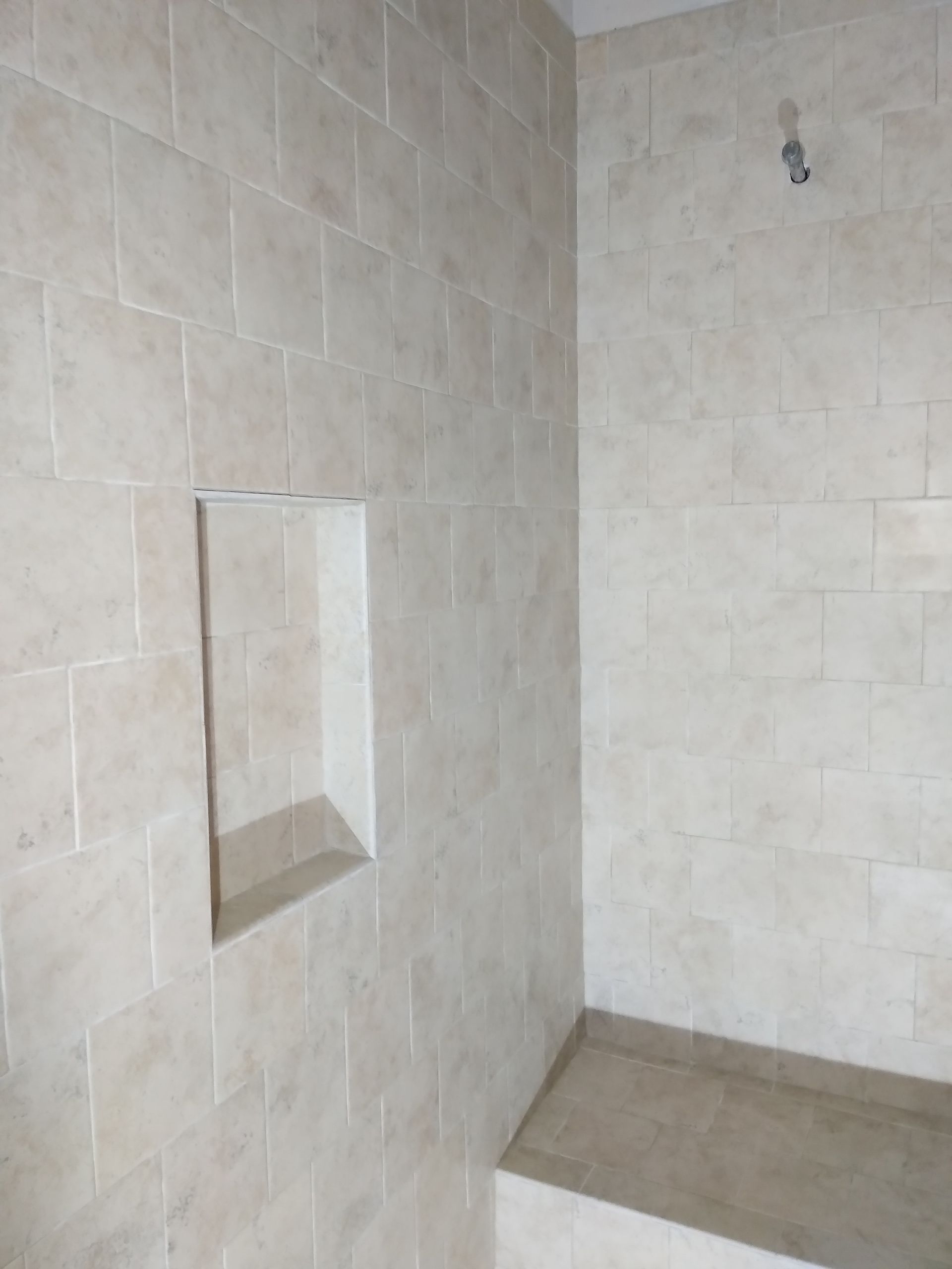 Empty beige tiled shower corner with a recessed niche and wall hook