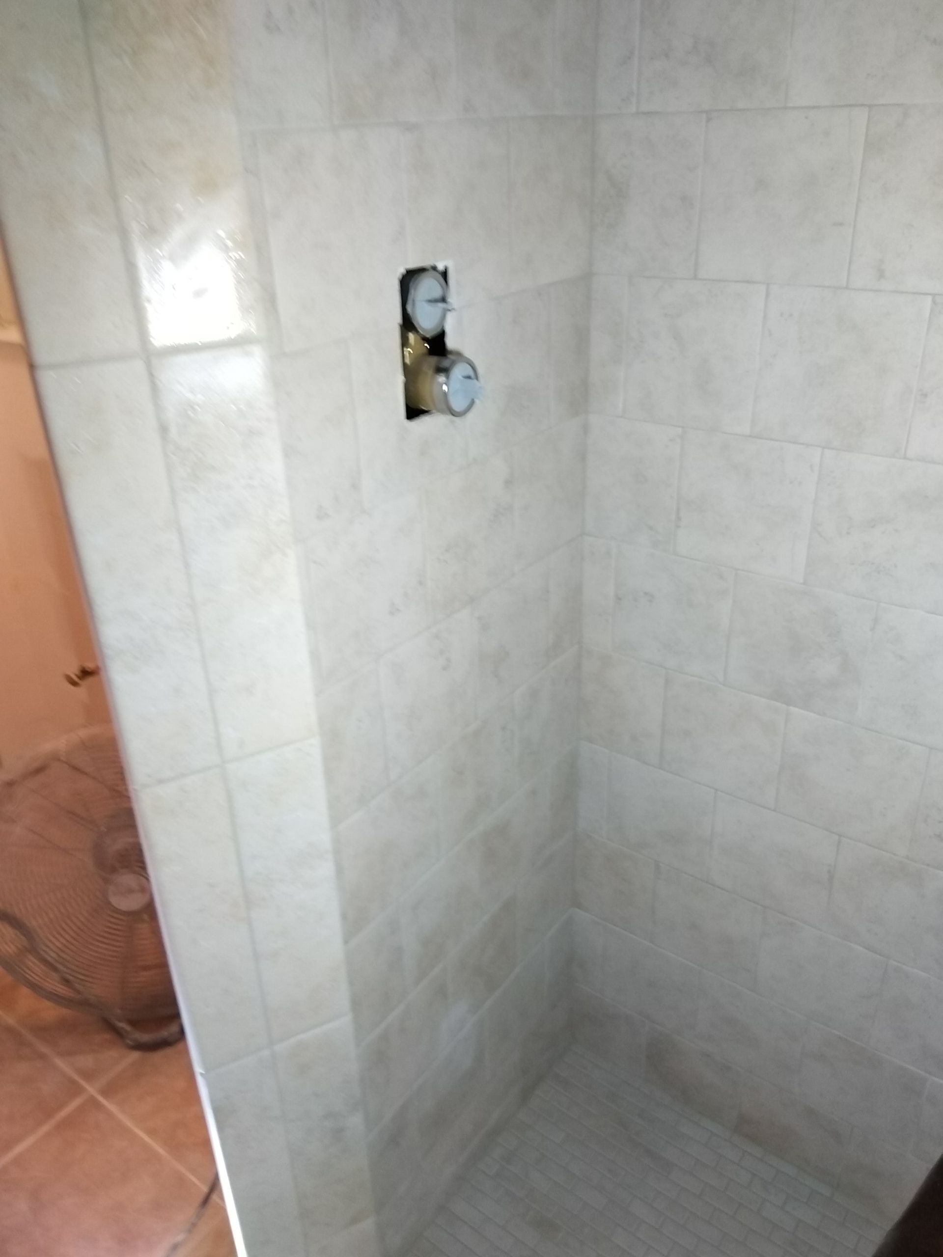 Empty tiled shower stall with a plumbing opening in the wall