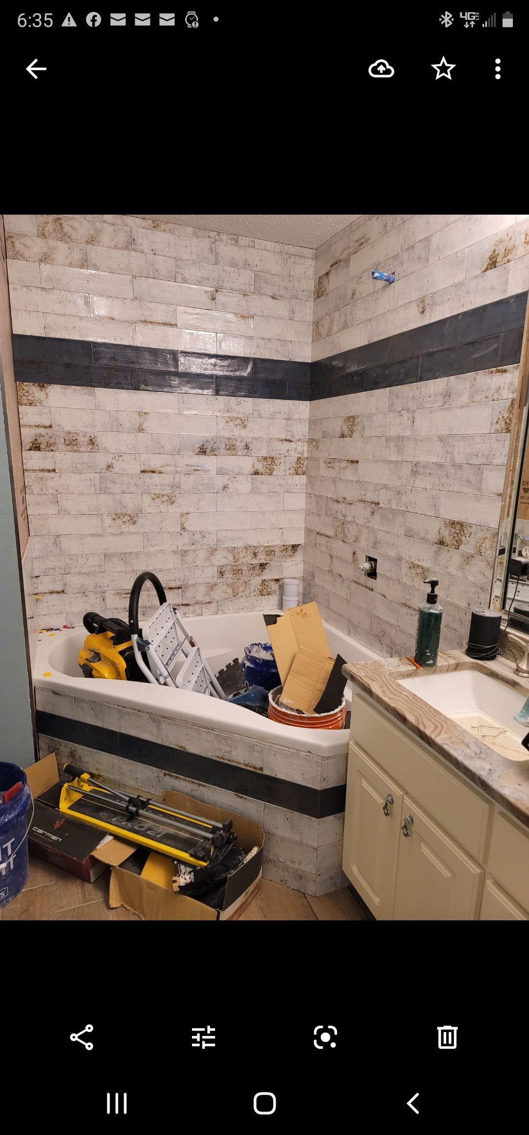 Small bathroom under renovation with a tub, white cabinets, and construction debris on the floor