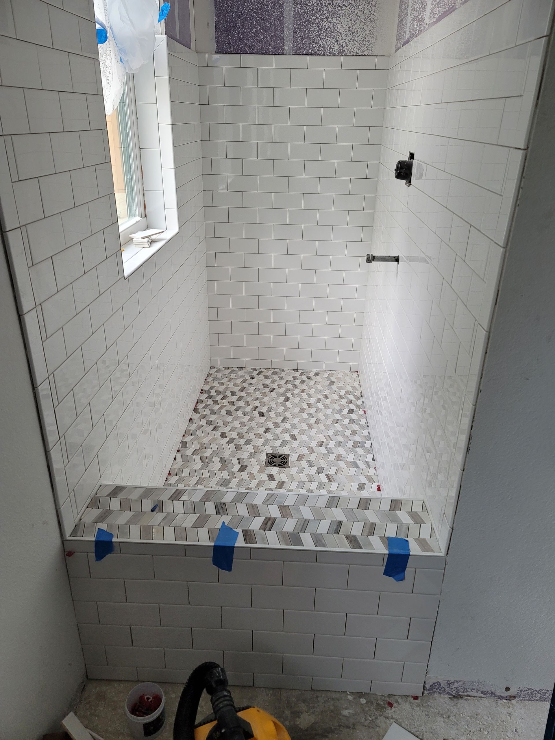 Partially tiled shower stall with mosaic floor, white walls, and a small window opening