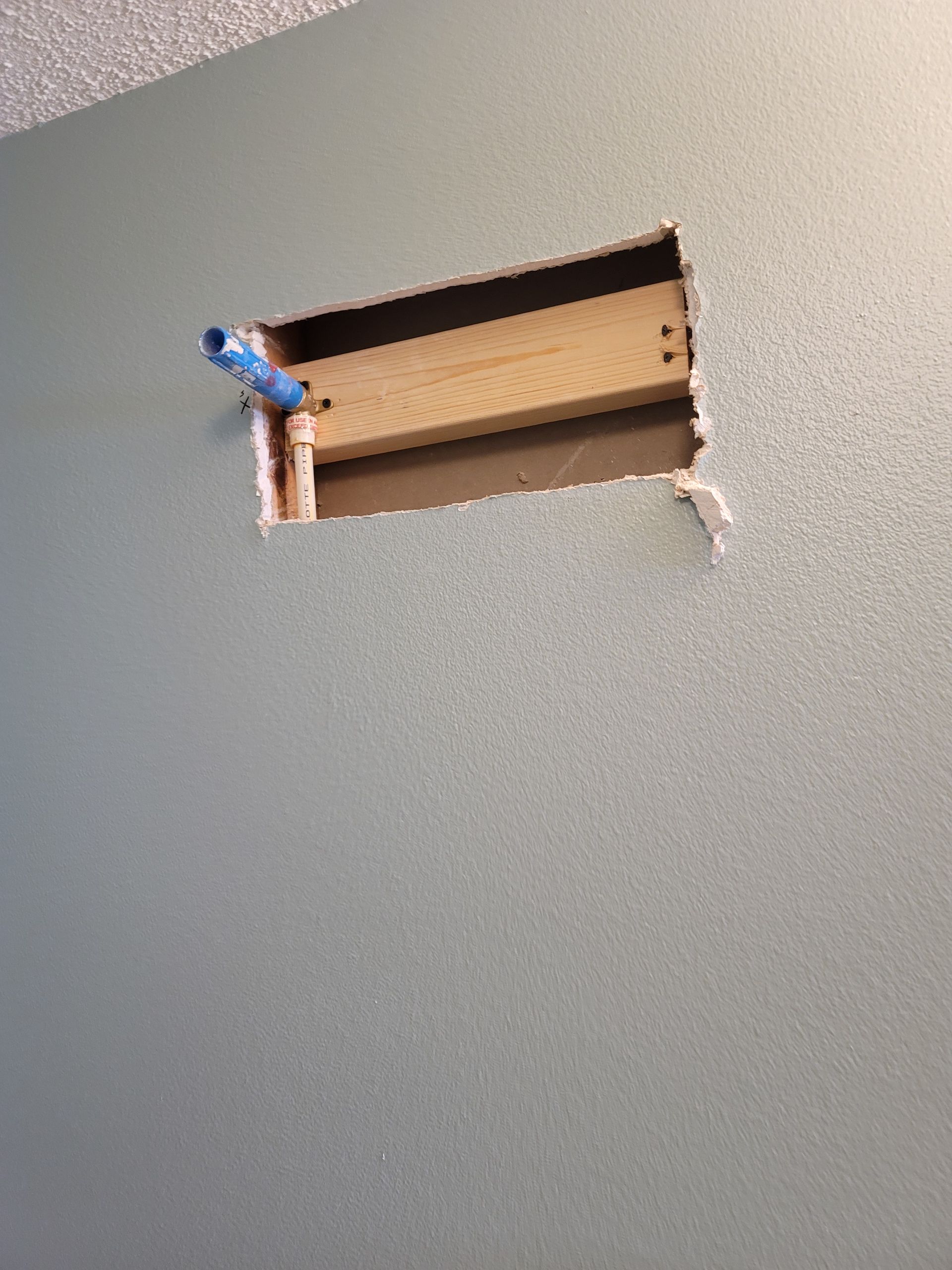 Damaged ceiling with a rectangular hole and exposed cardboard backing