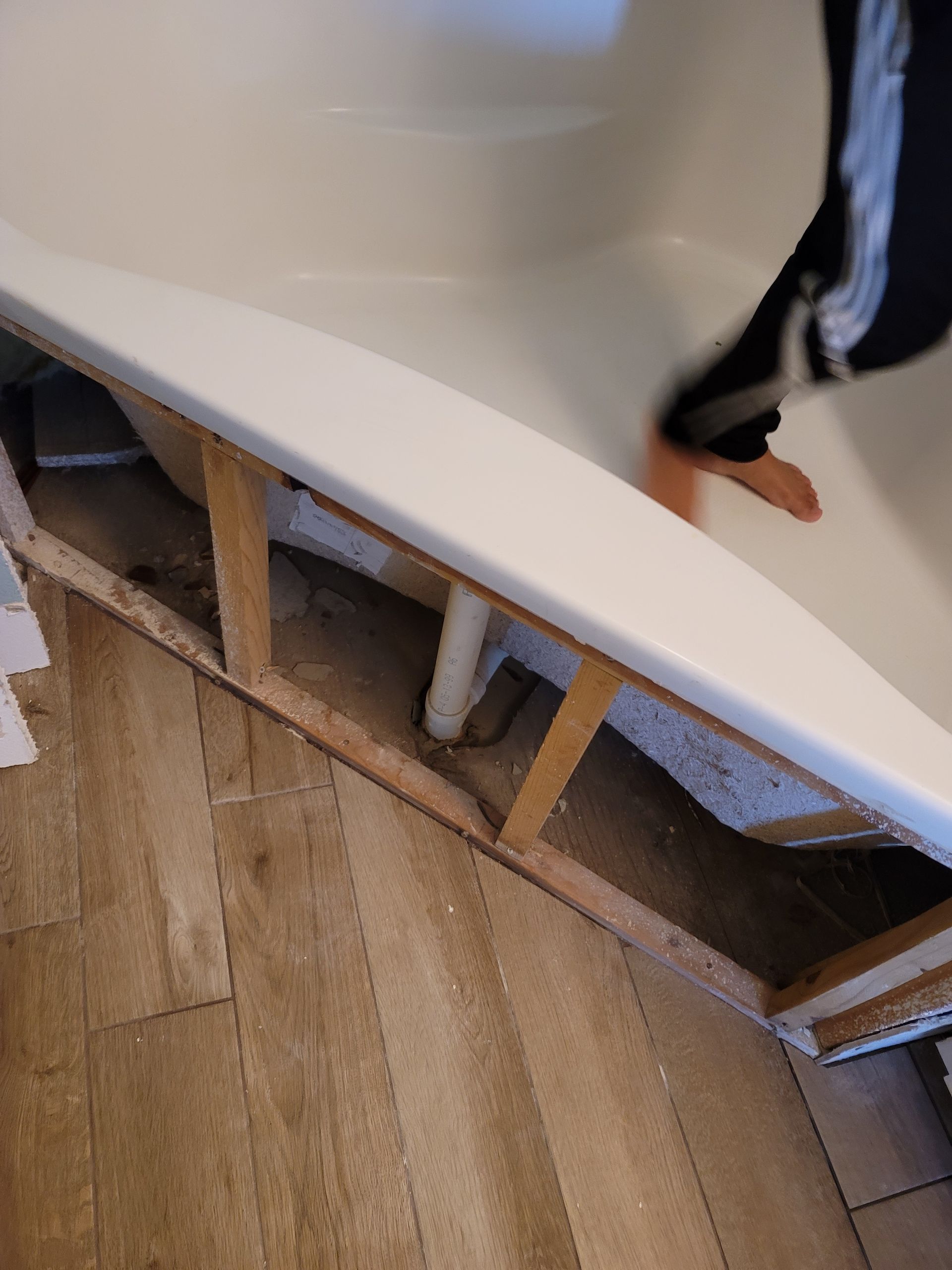 Broken white curved panel exposing wooden supports on a wood floor, with a person standing nearby