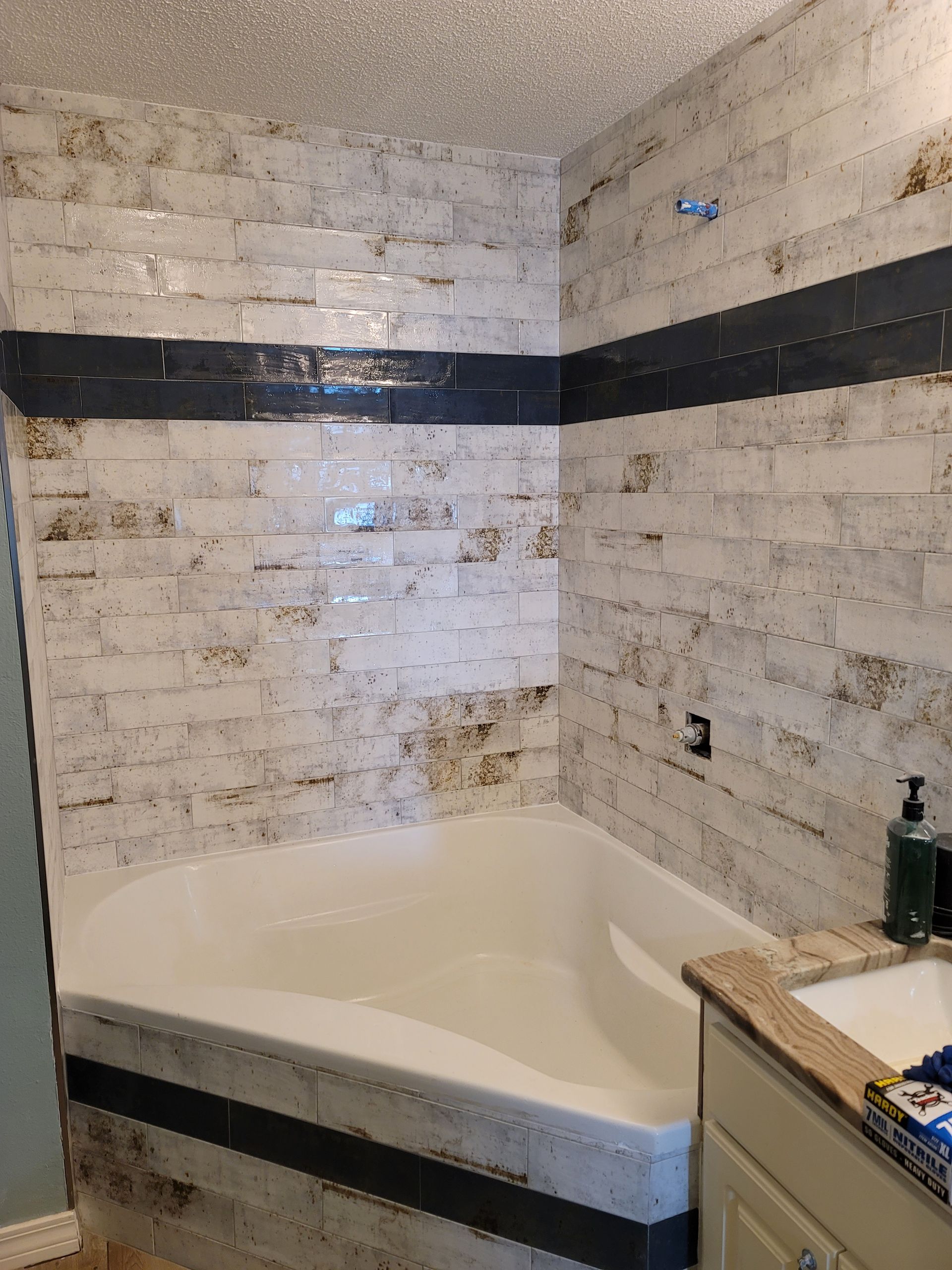 Small bathroom with a white corner tub, tiled walls, and a black horizontal accent band.
