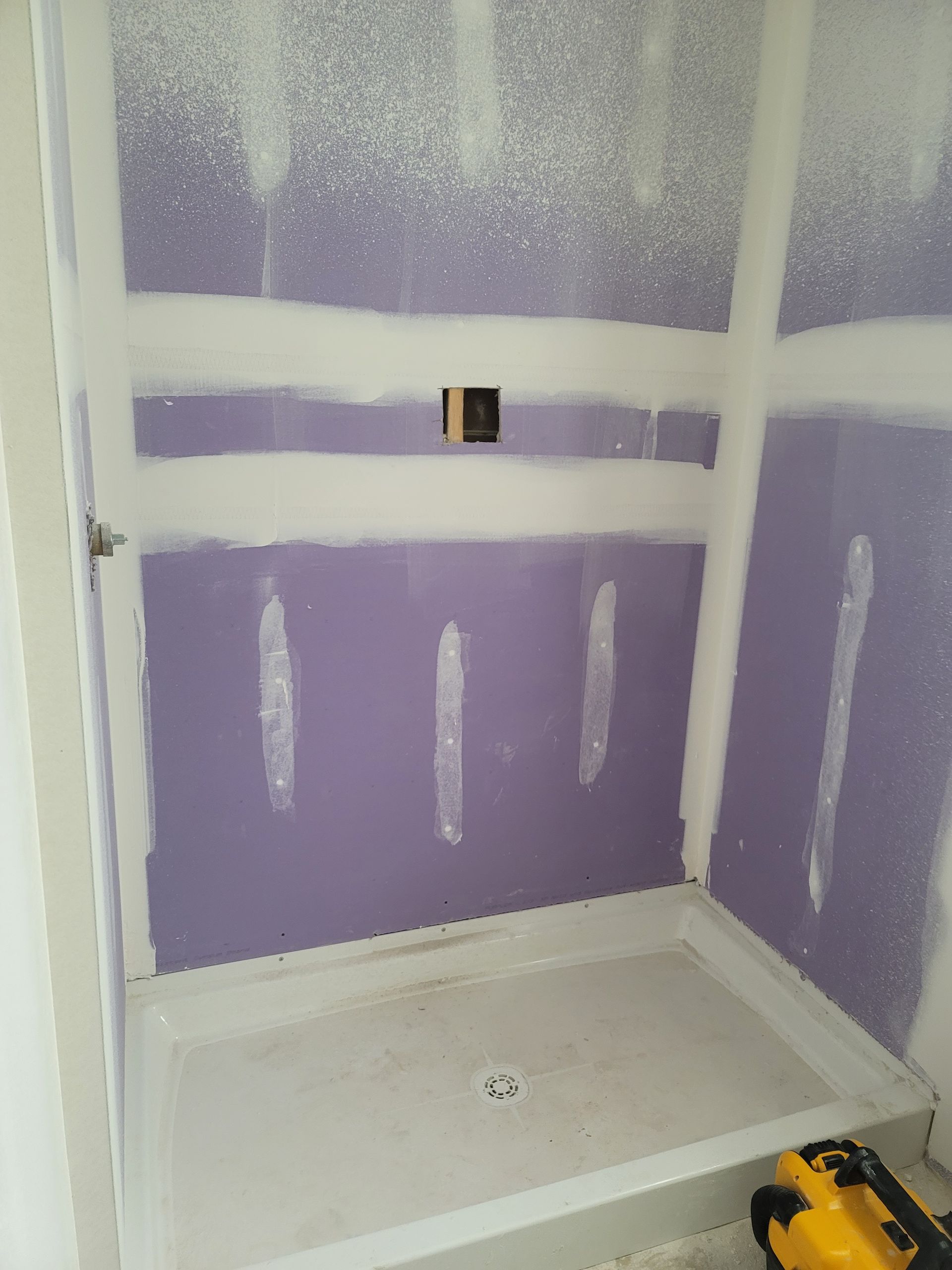 Purple drywall in a tiled shower or bathroom under construction, with a shower pan and drain.