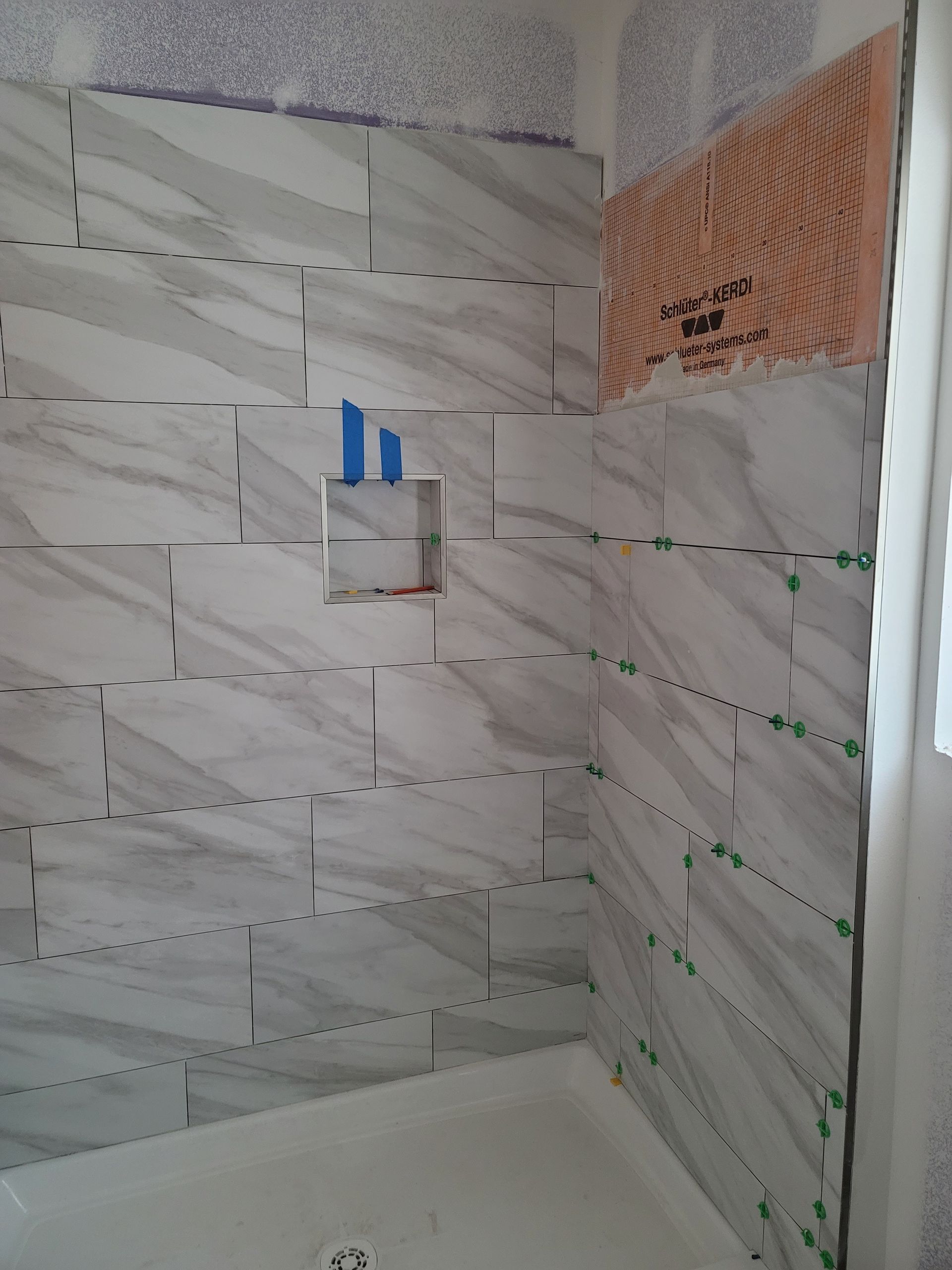 Tiled shower corner with a small blue-and-white fixture on the wall and a white shower base.