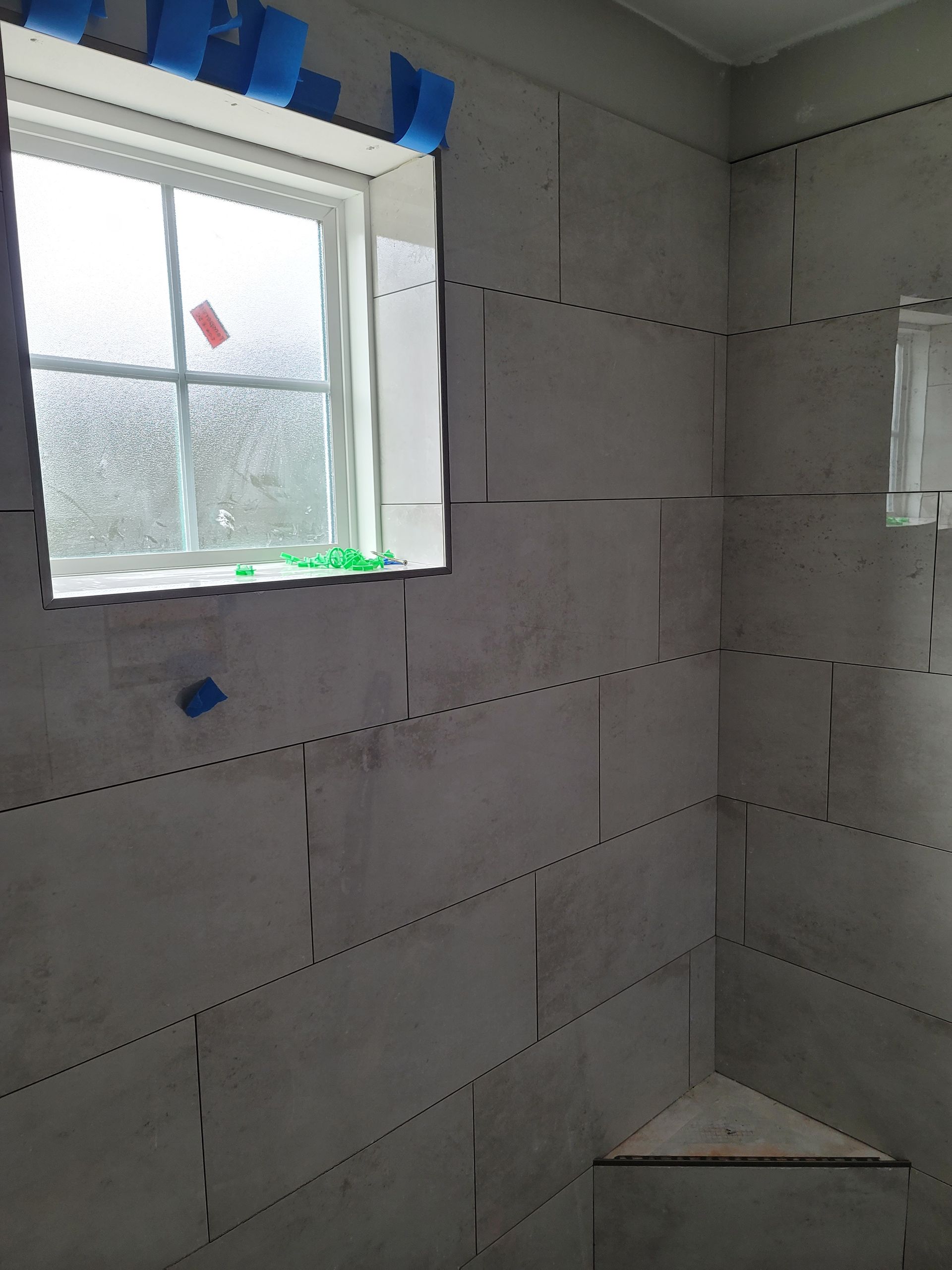 Unfinished tiled bathroom with a window and a shower base under construction.