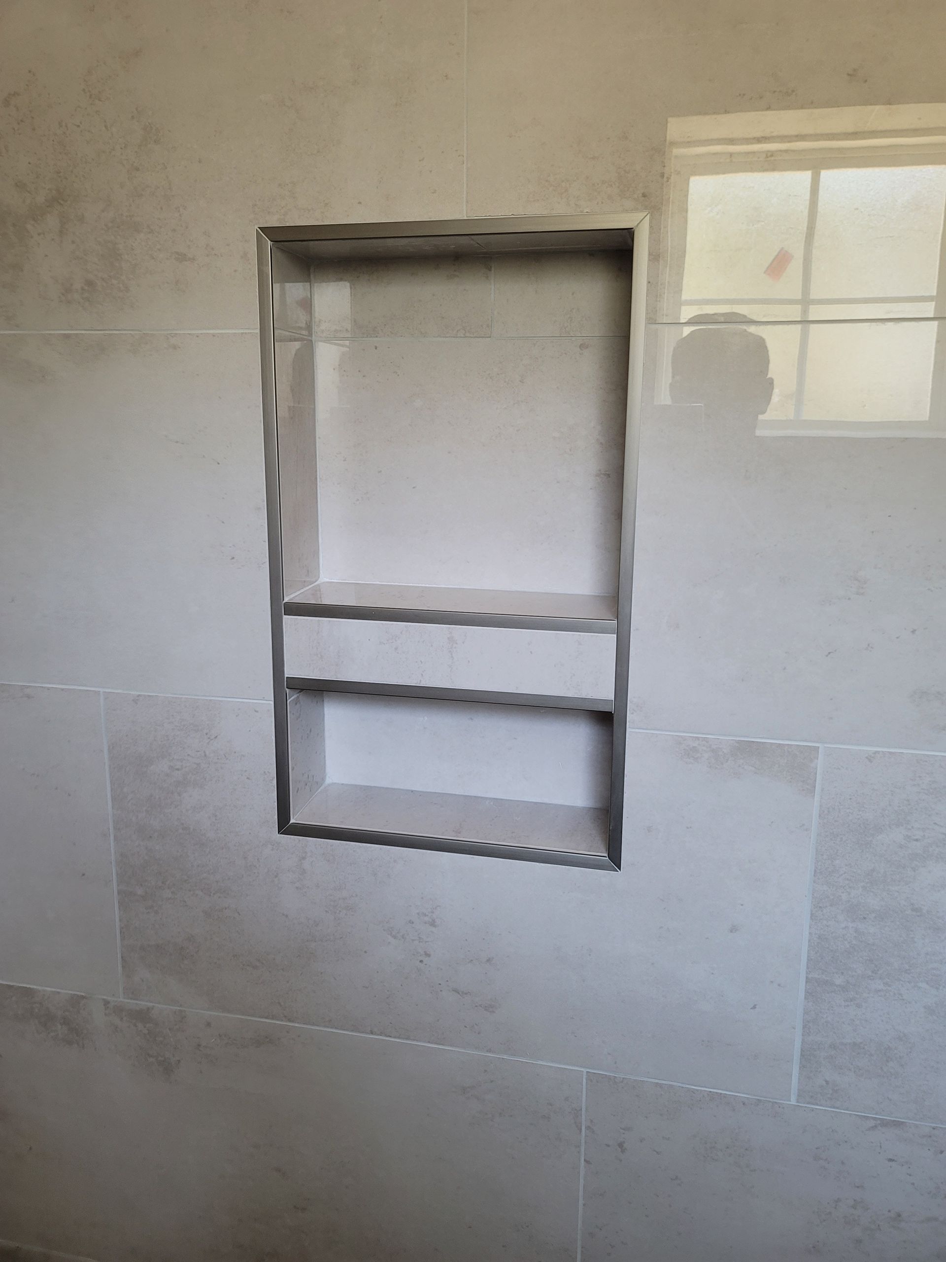 Unfinished wall niche with exposed framing and a small window reflection on a plastered interior wall