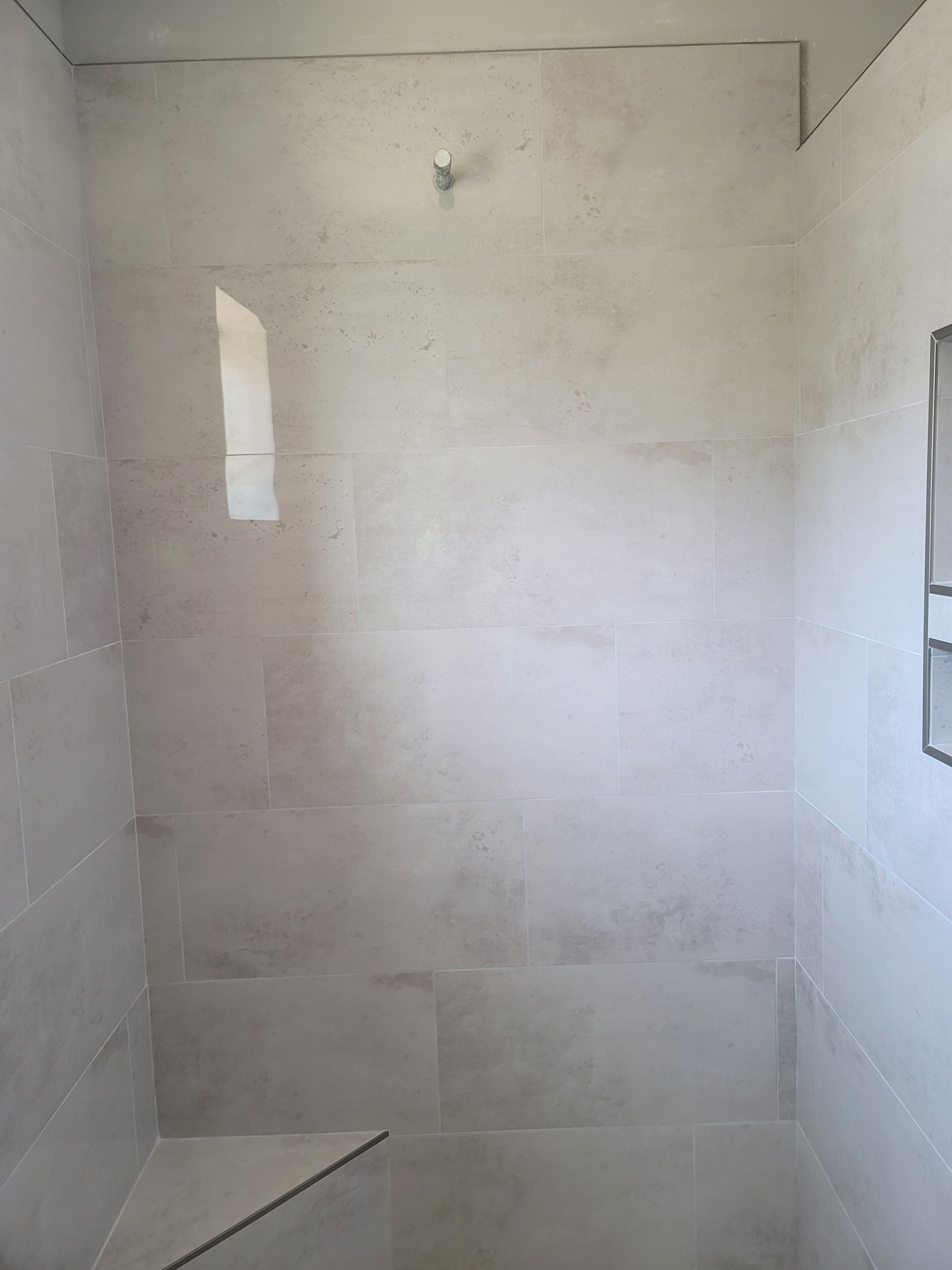 Empty tiled shower stall with white walls and a built-in shelf.