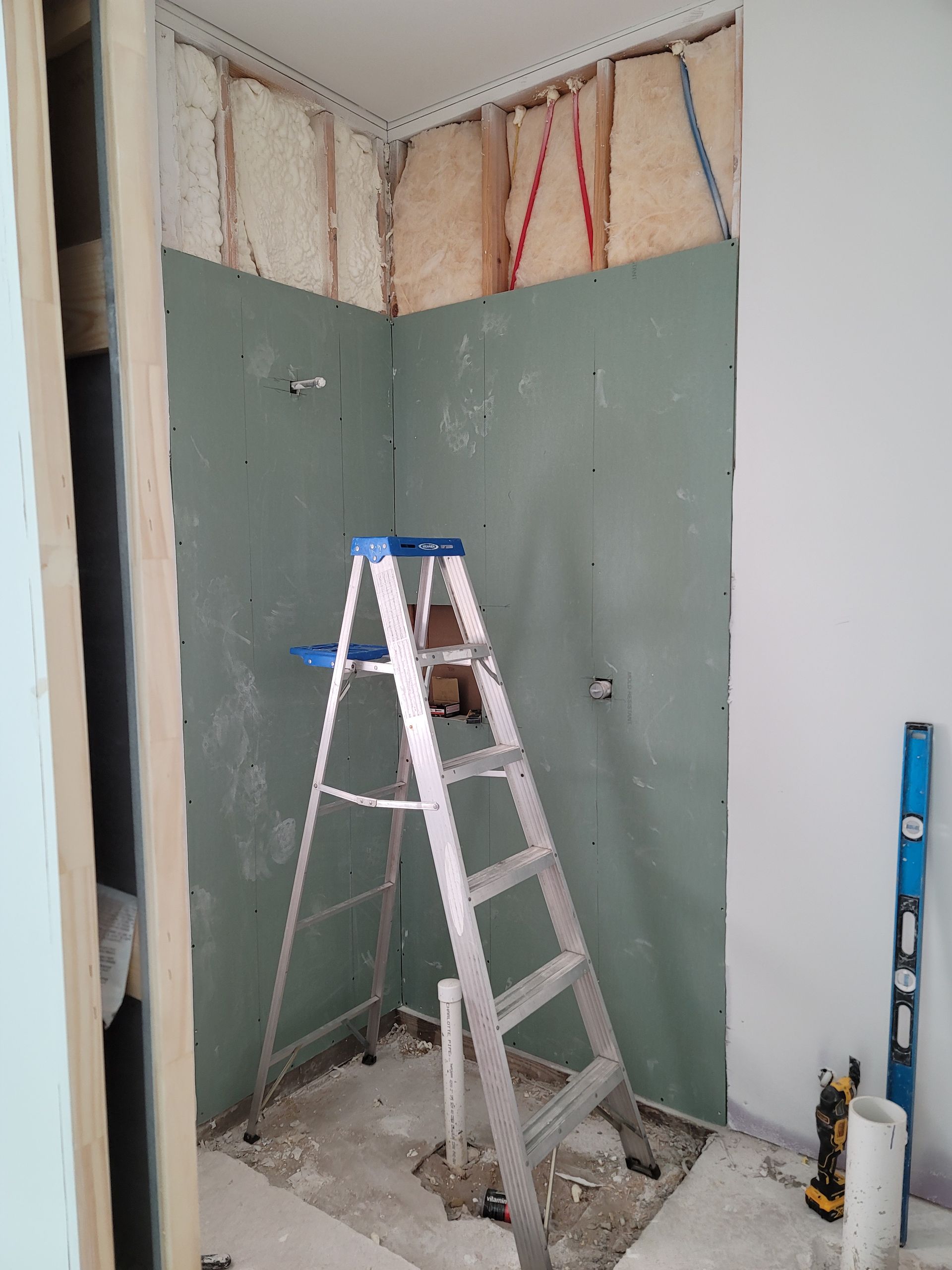 Small unfinished closet with ladder, exposed insulation, and green drywall being installed.