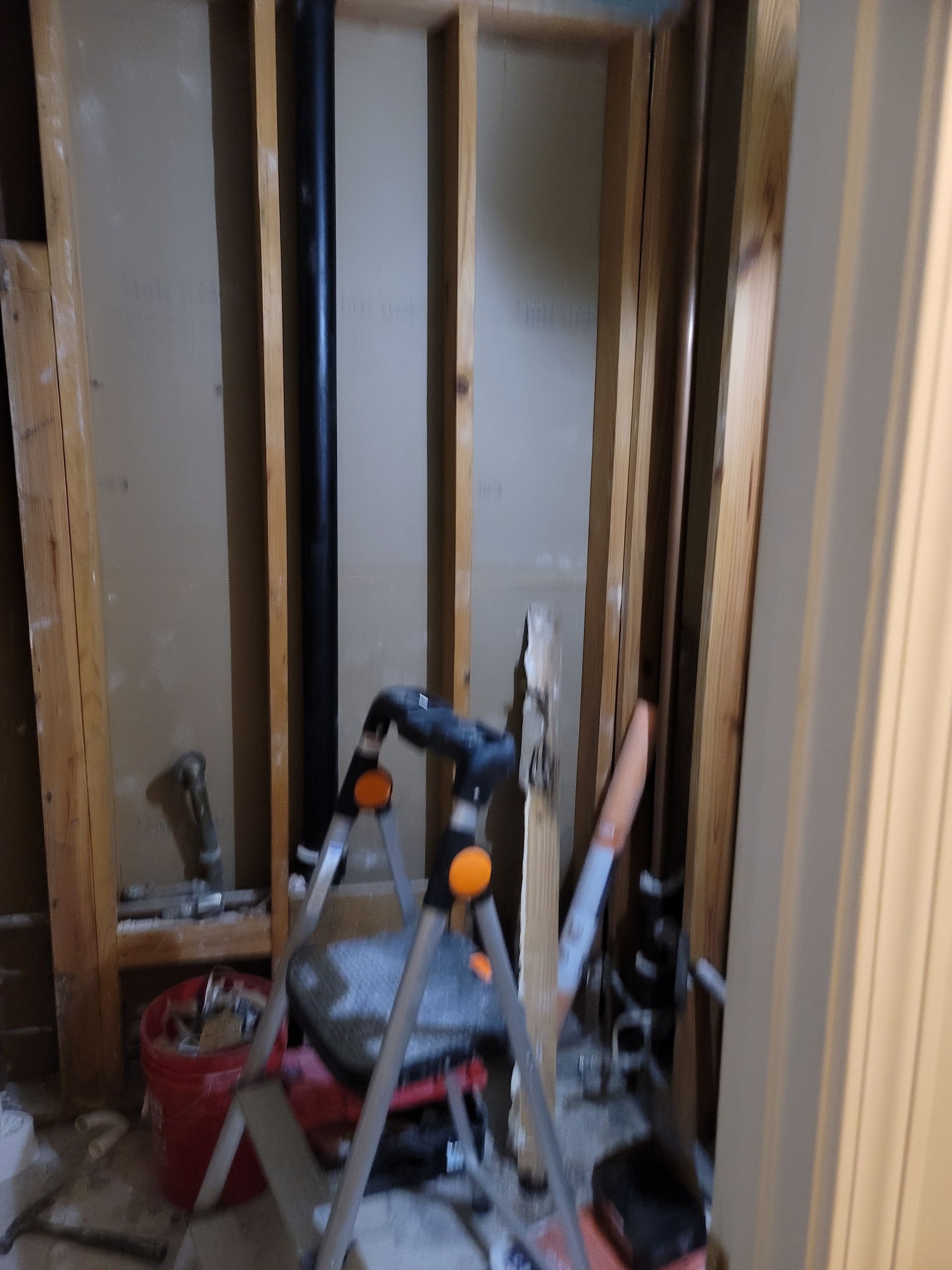 Narrow unfinished hallway with exposed studs and tools, including a step ladder and work materials.