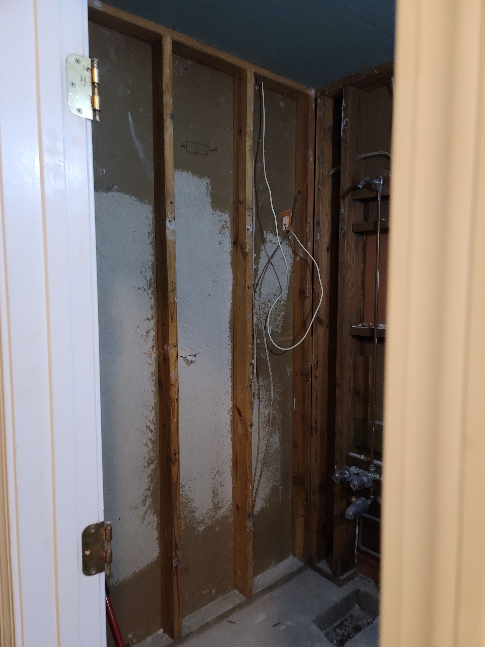 Partially open doorway to a narrow room under construction with exposed studs and wiring.