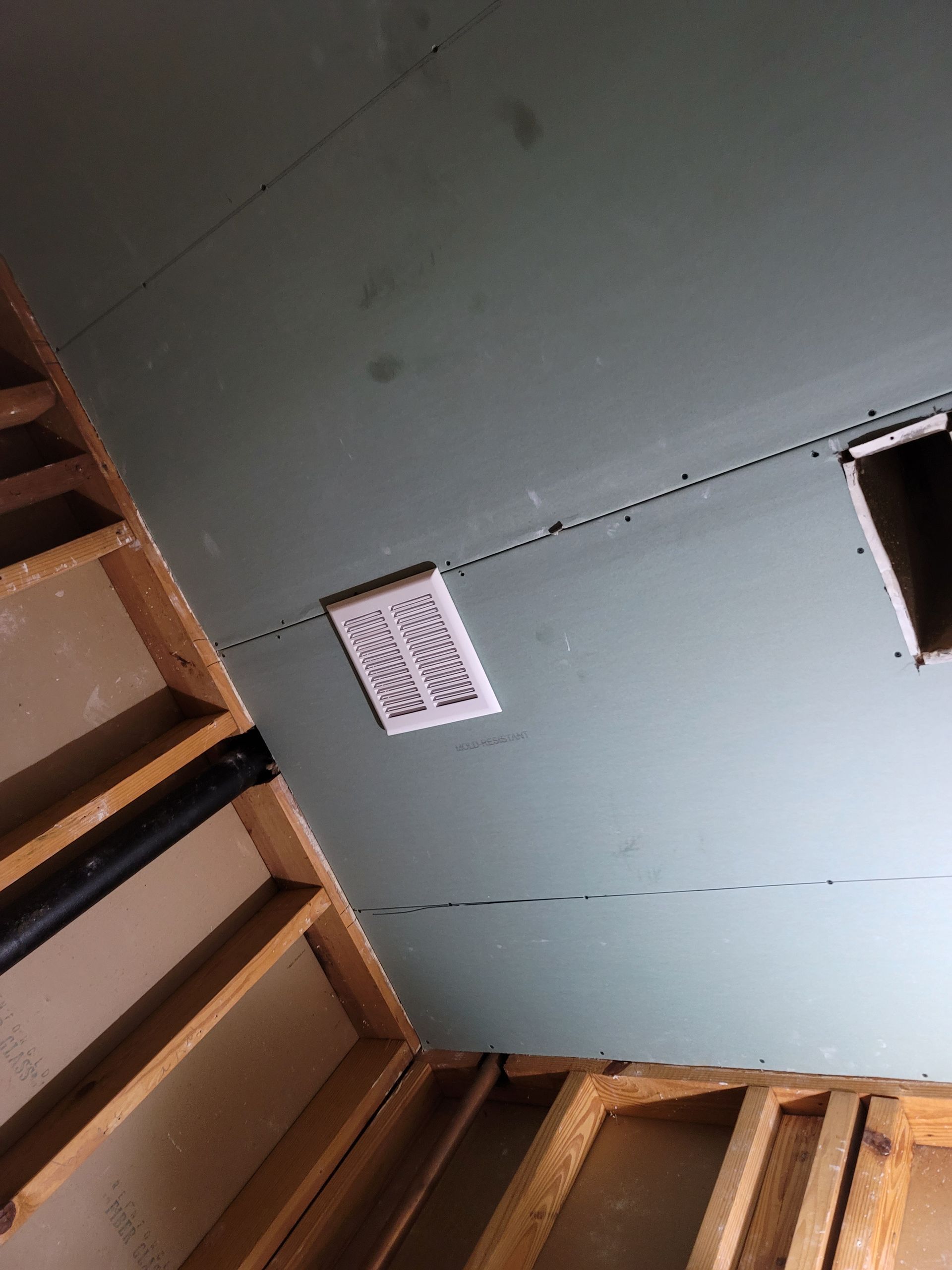 Rotated view of a stairwell under construction with exposed wood framing and a vent on a pale wall