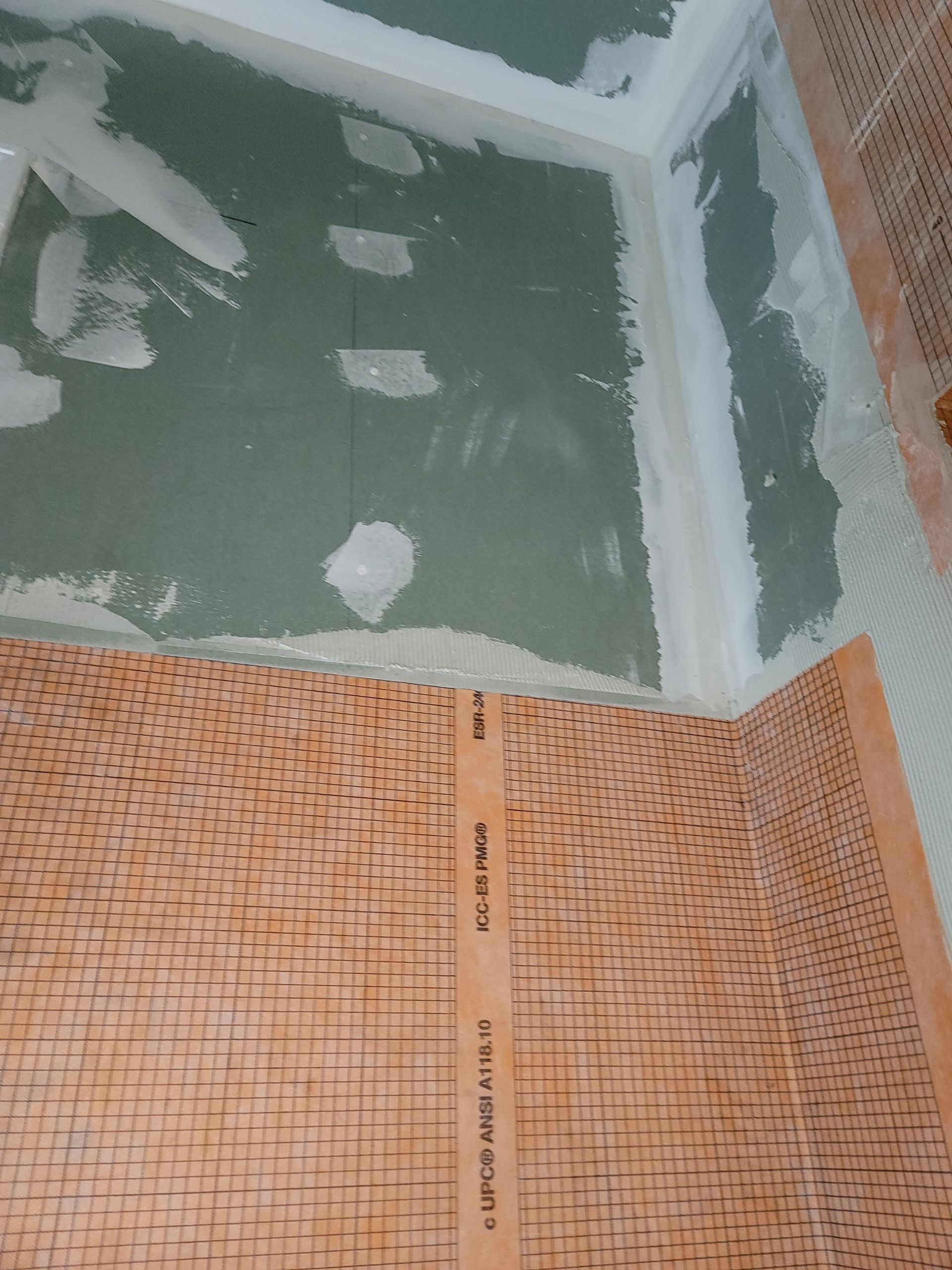Partially tiled wall corner with green waterproofing and orange mosaic tile sheets during renovation