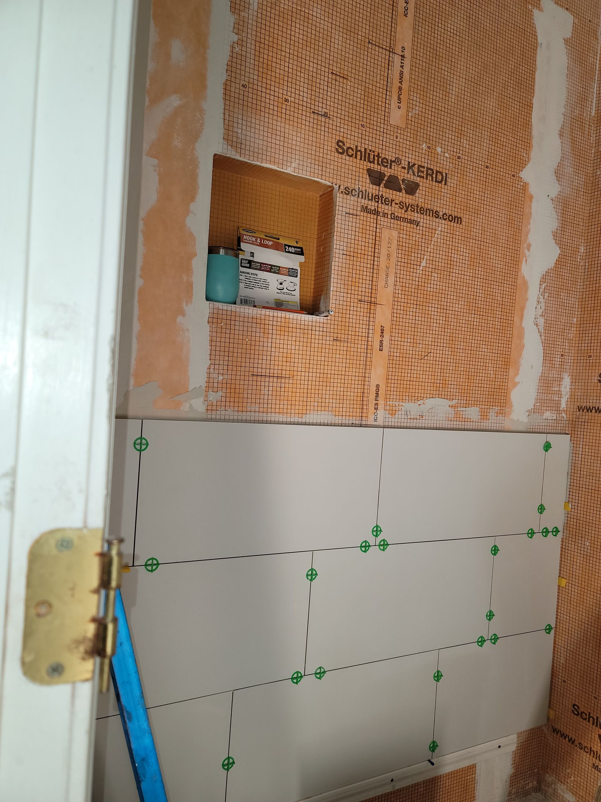 Partially tiled wall with exposed orange insulation and a small electrical box near a door frame