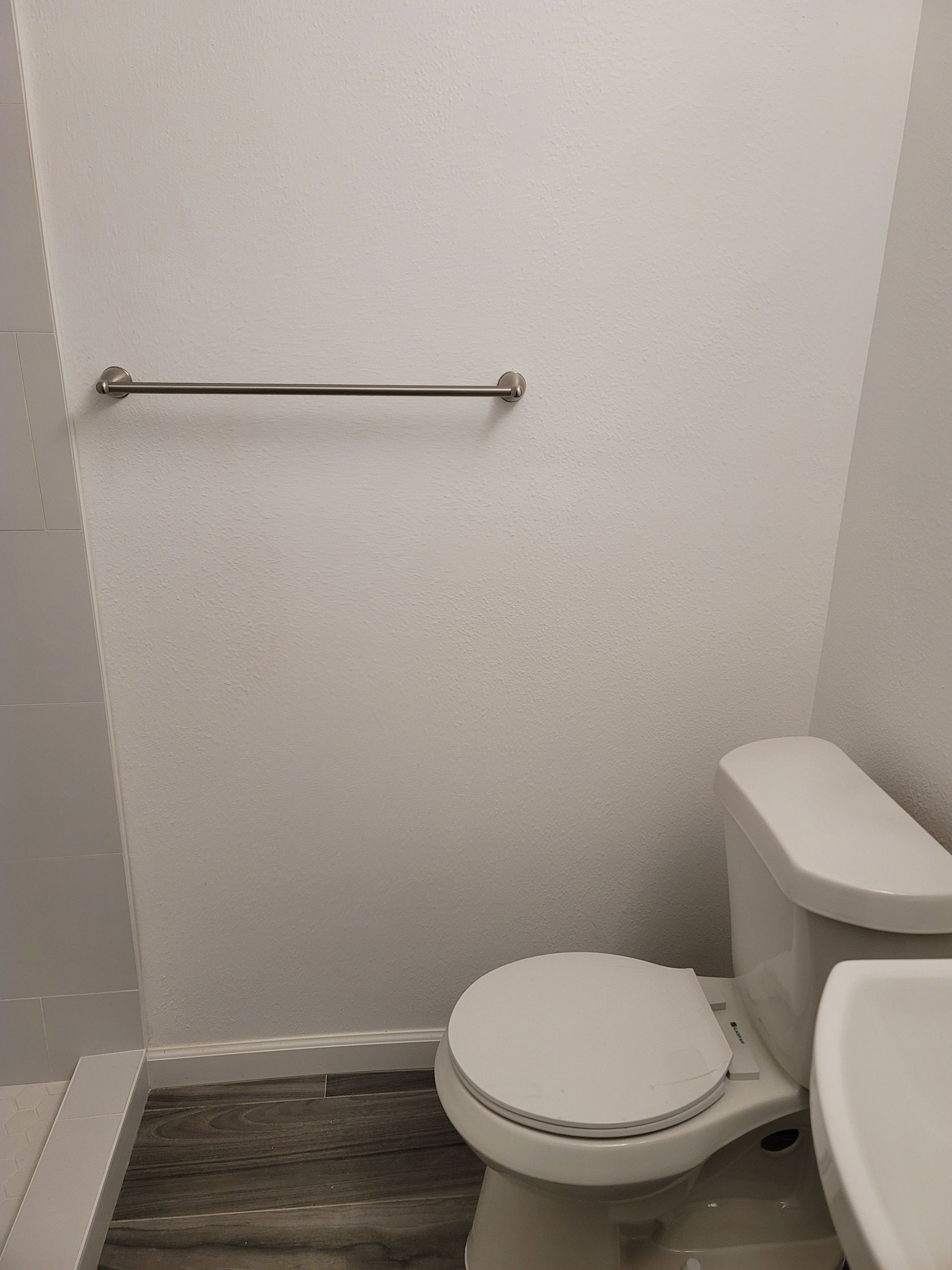 Small bathroom with toilet, white walls, and a metal grab bar.