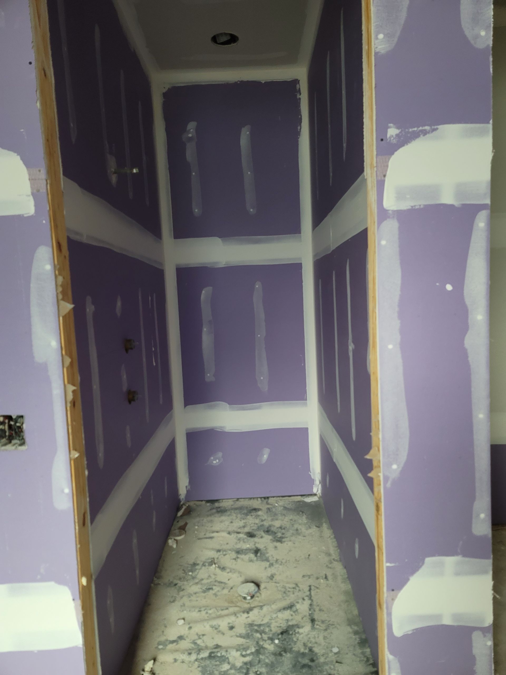Unfinished closet or pantry with purple drywall, white patches, and dusty floor.