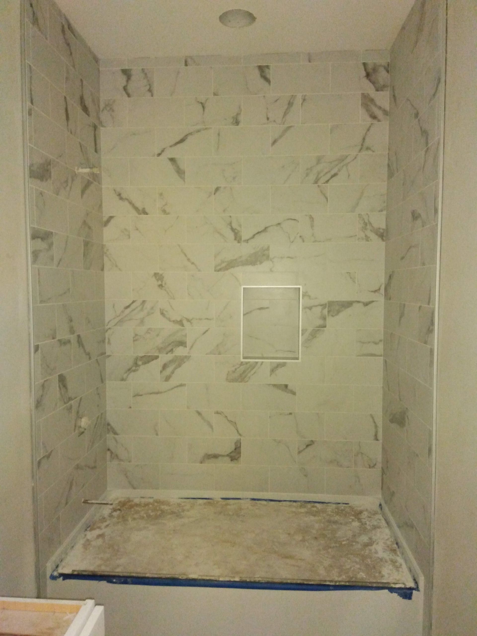 Small tiled shower stall with a drain, beige walls, and a recessed soap dish.