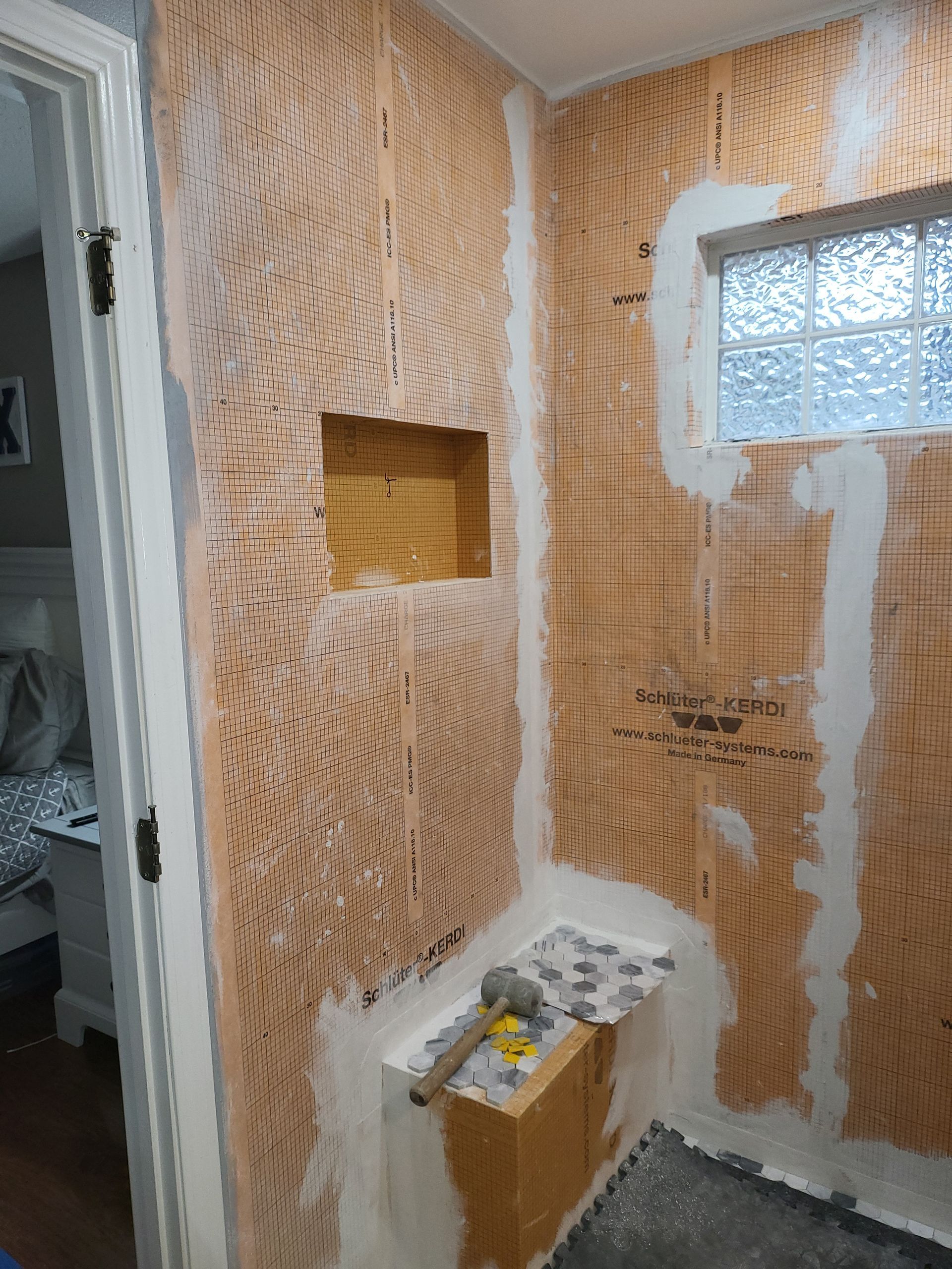Partially renovated room with exposed plywood walls, window, and a small wall shelf with tools and supplies