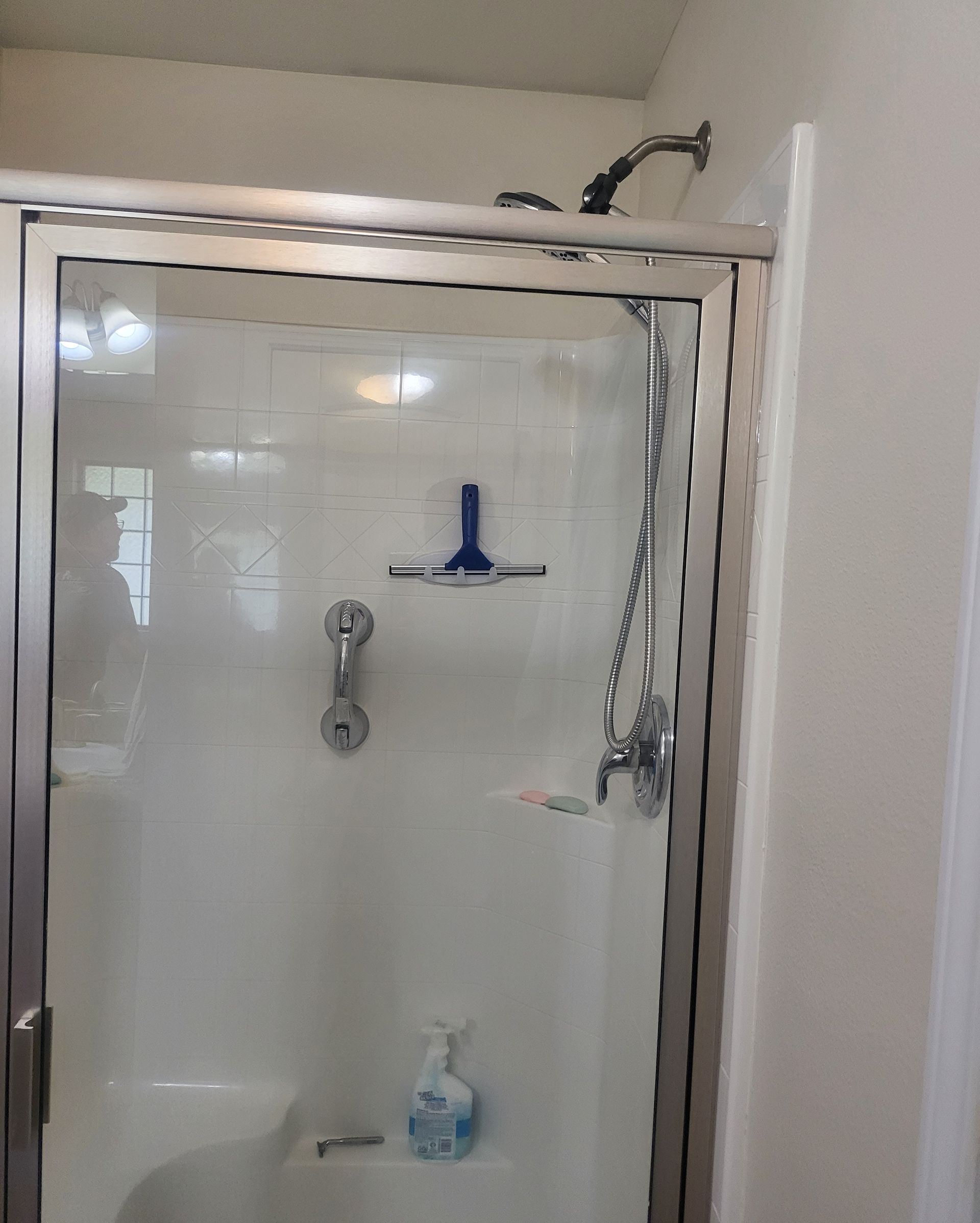 Small bathroom shower stall with white walls, a blue squeegee, and a hanging silver shower caddy.