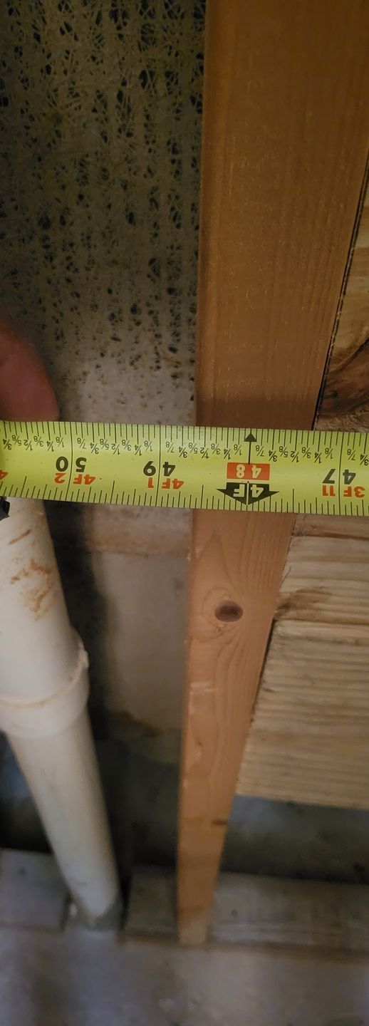 Yellow tape measure stretched across exposed wooden framing next to a white pipe and wall insulation.