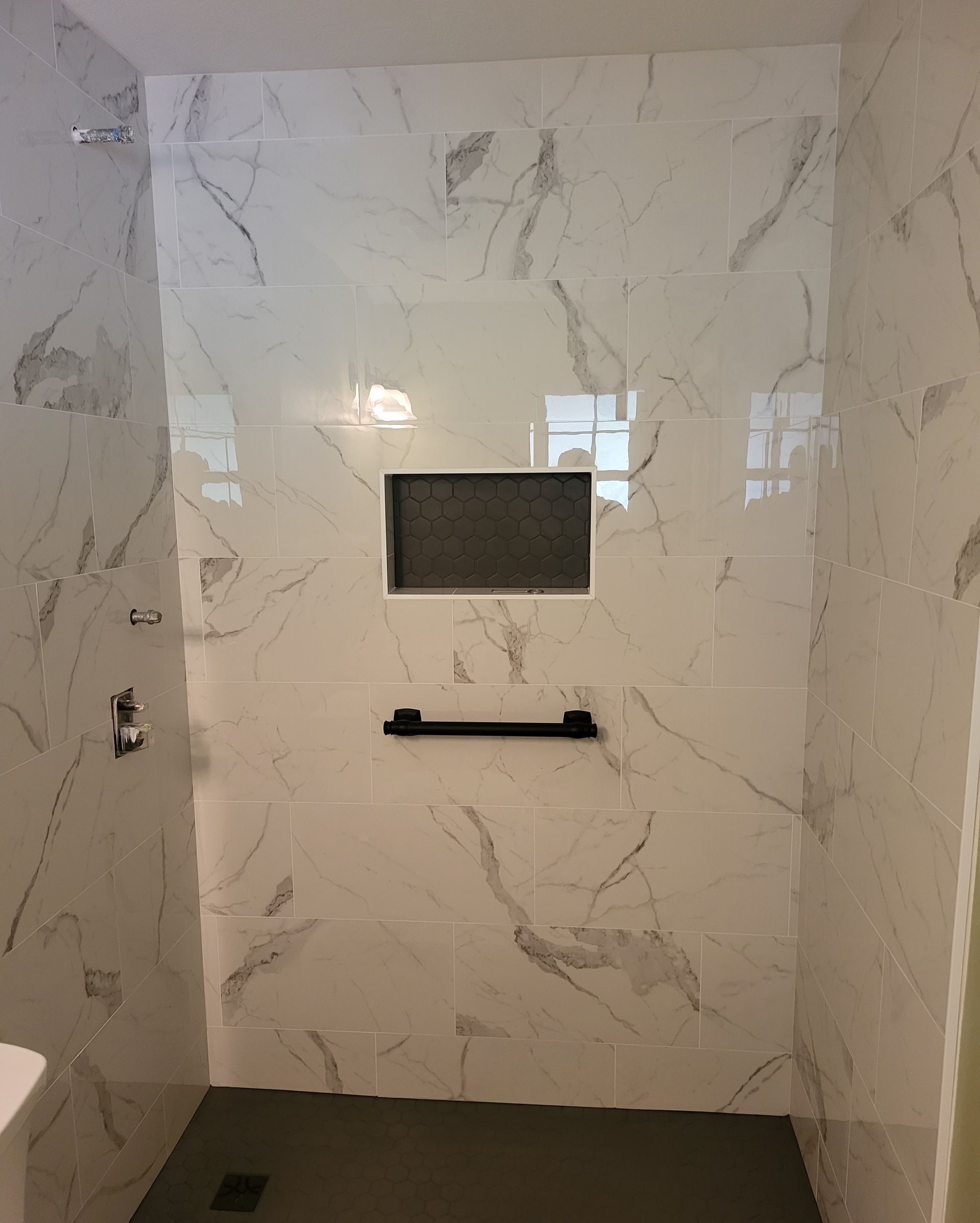 Modern tiled shower with a small window and black shelf.