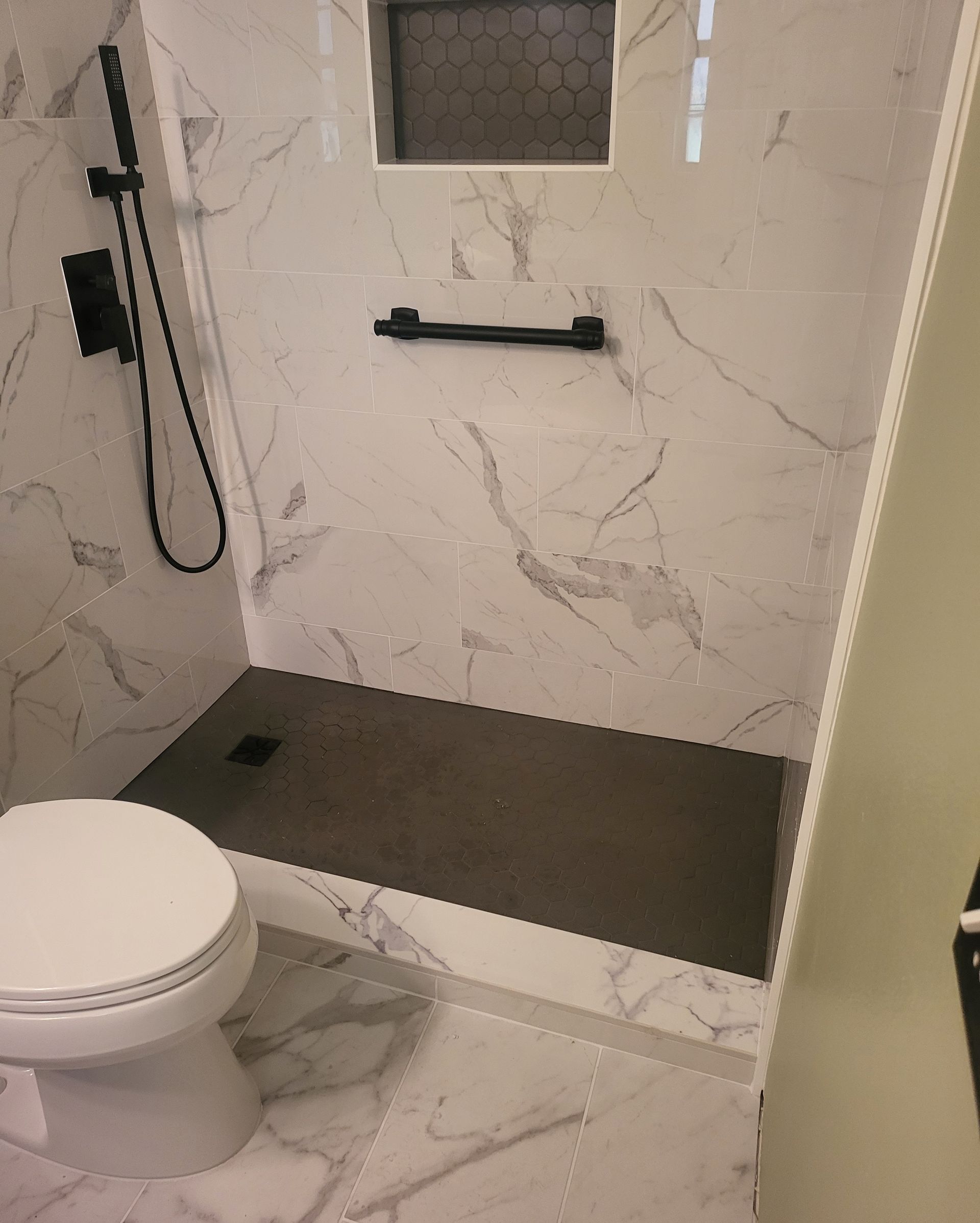 Modern shower with marble-look walls, black fixtures, bench, and adjacent toilet.