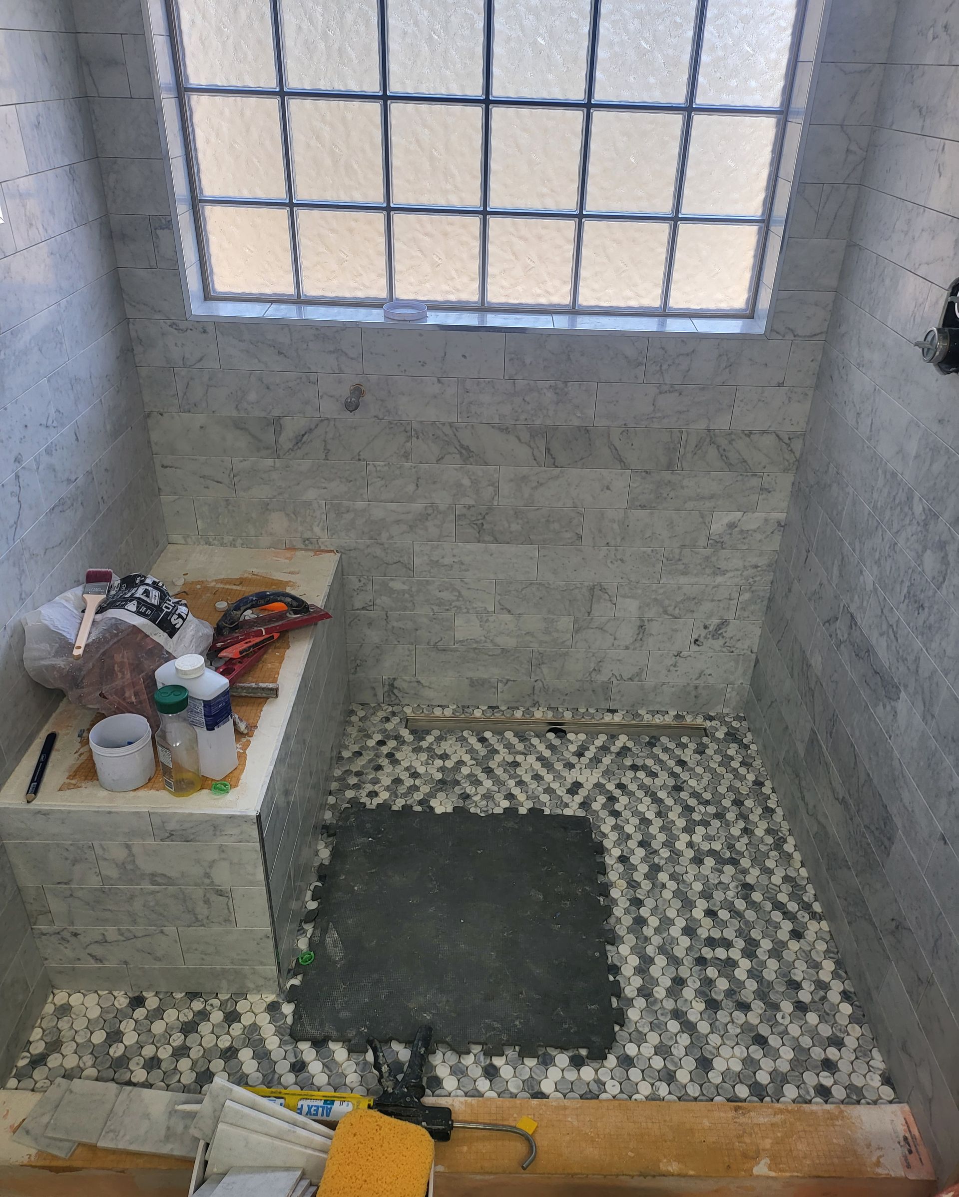 Small tiled bathroom with a window, a low toilet, and cleaning items on a shelf.