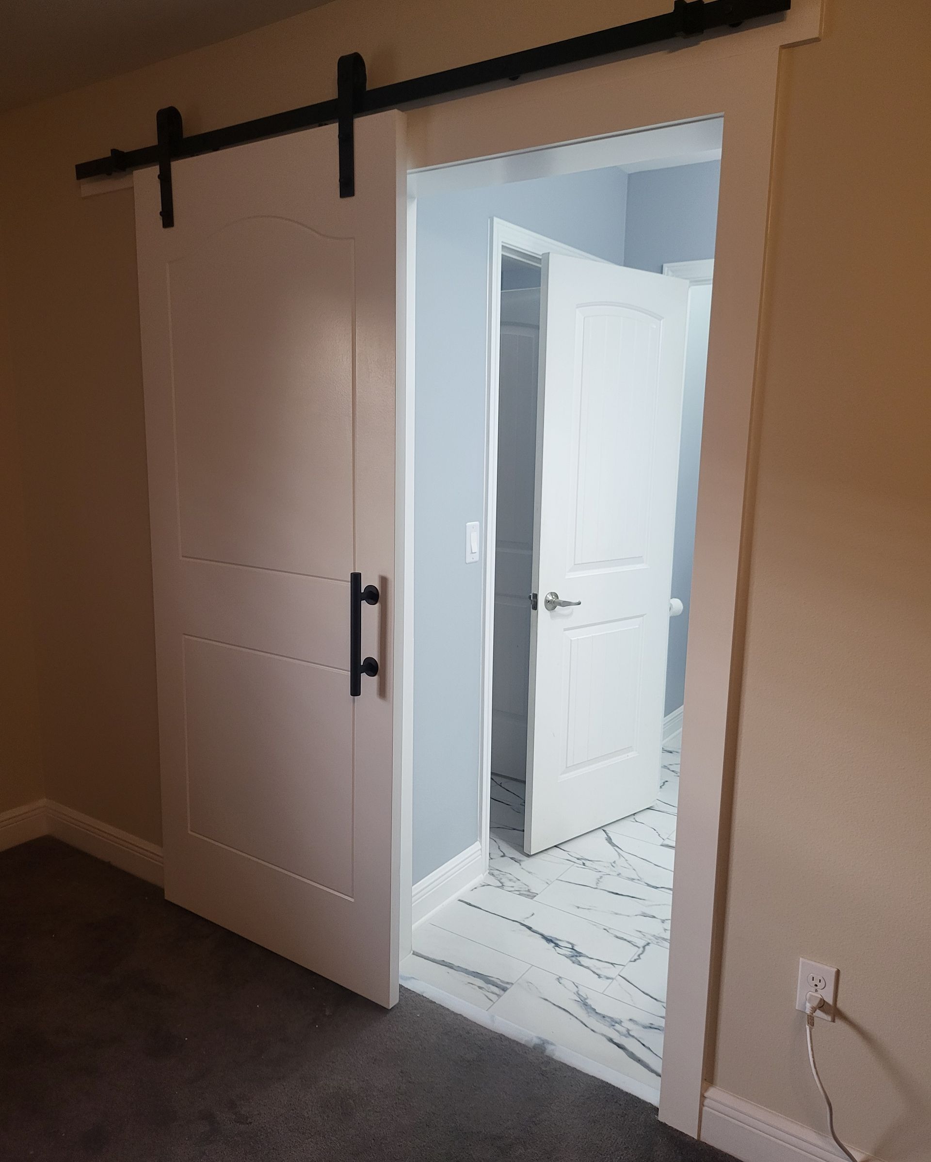 Open white barn door on a dark track, revealing a bright hallway and another open door inside.