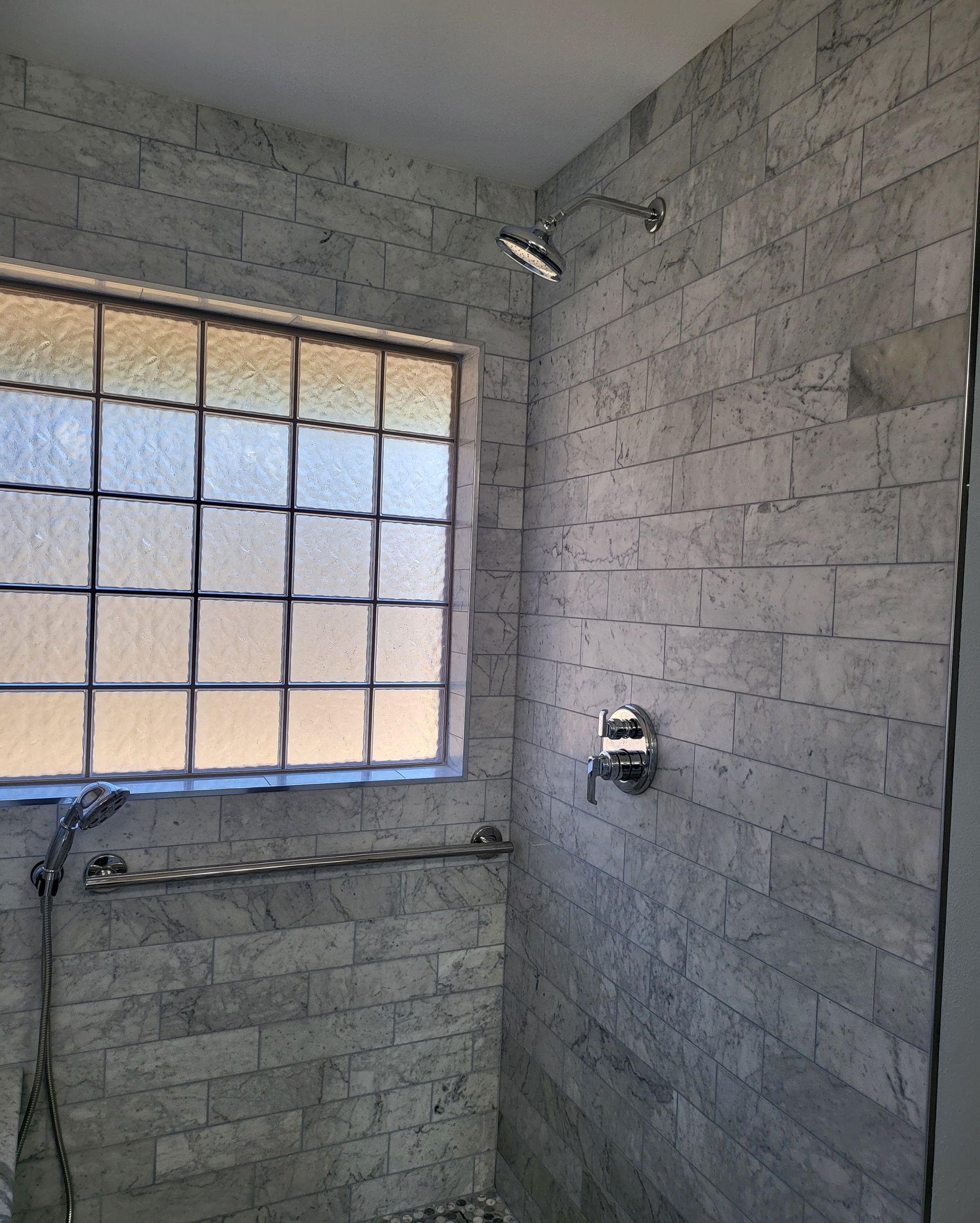 Shower with gray tile walls, small window, and chrome fixtures in a bathroom