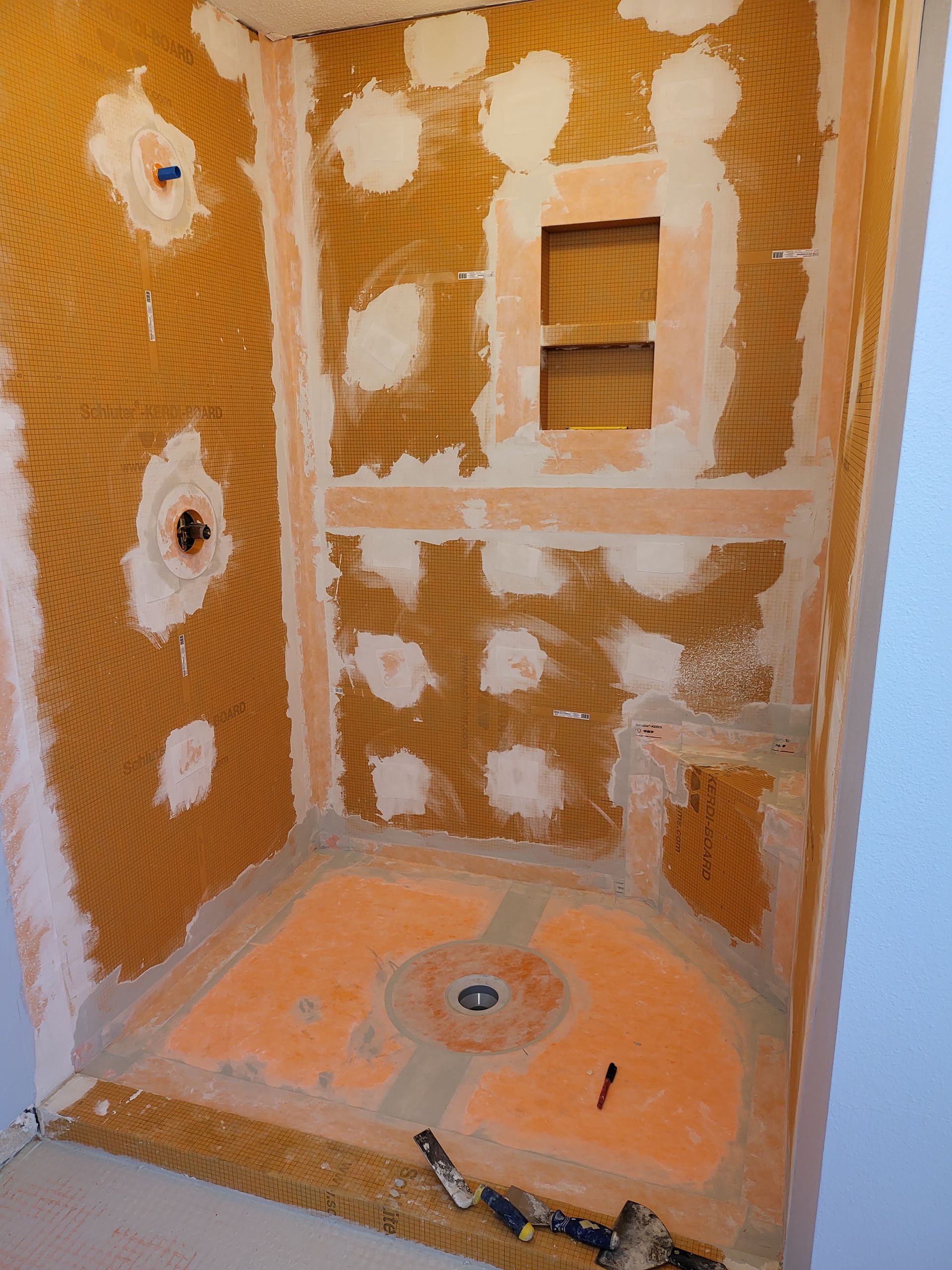 Unfinished shower stall with orange waterproofing, tile backer, and a shower pan drain